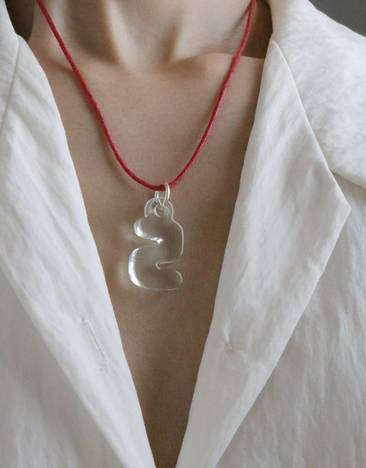 Bubble-shaped transparent glass Letter Charm | 한글 Hangul pendant on a red cord necklace, worn against a white shirt, symbolizing Korean language and culture. Eco-friendly jewelry made from recycled window glass by CLED.