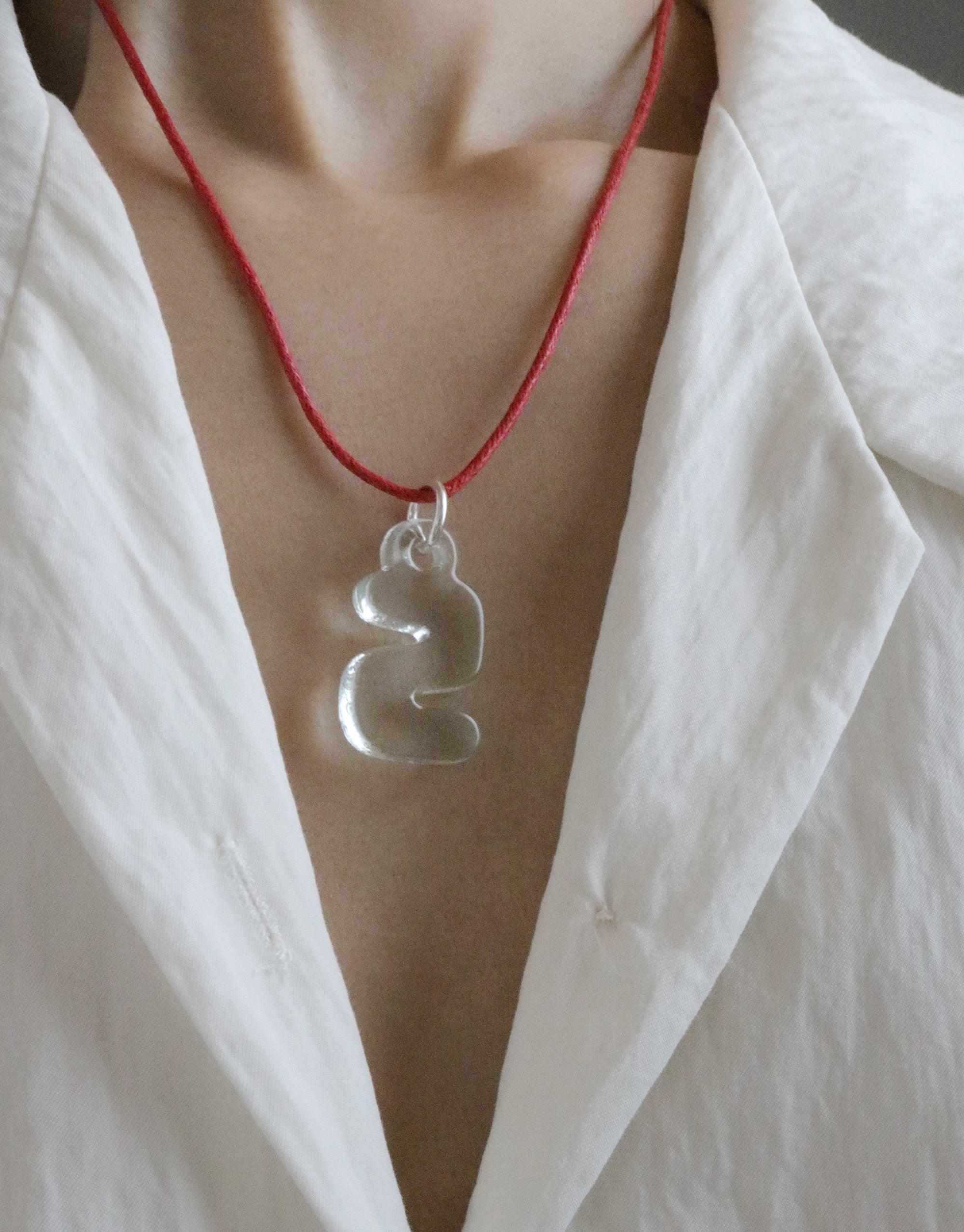 Bubble-shaped transparent glass Letter Charm | 한글 Hangul pendant on a red cord necklace, worn against a white shirt, symbolizing Korean language and culture. Eco-friendly jewelry made from recycled window glass by CLED.