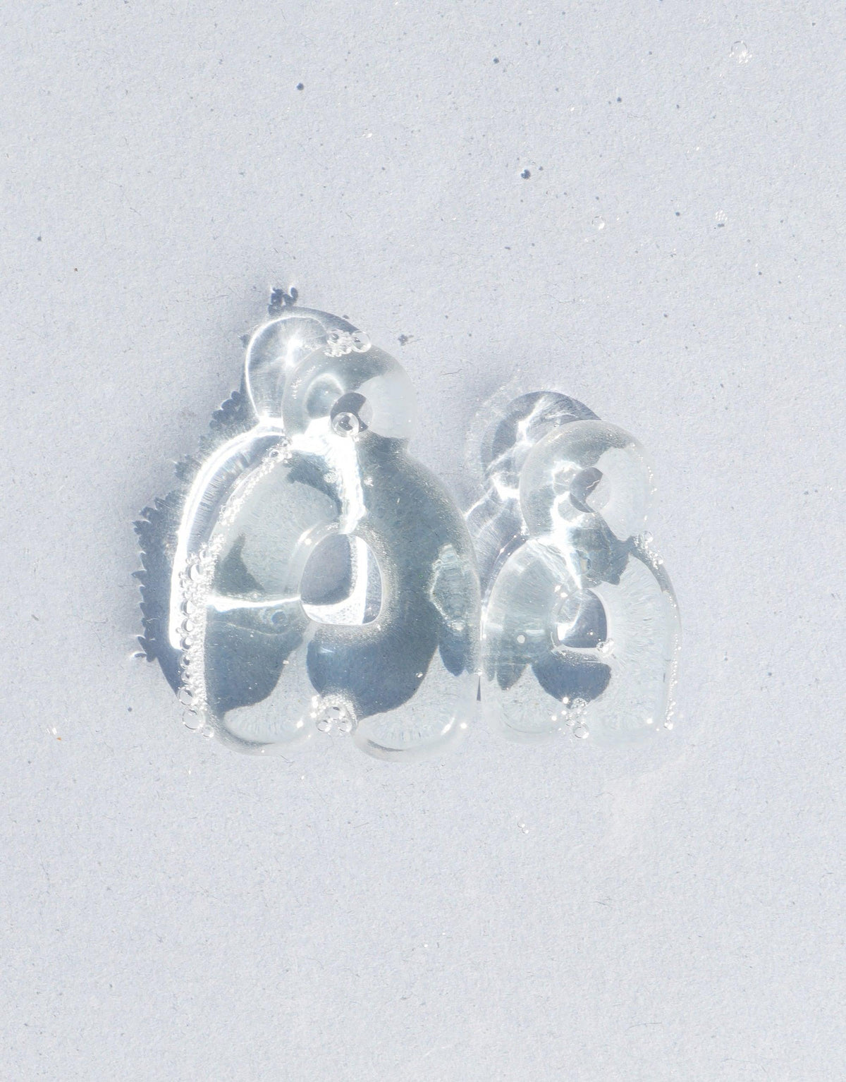 Transparent bubble-like letter charms 'C' and 'D' on a light background, showcasing the rounded, playful design of the Letter Charm | Alphabet product. Eco-friendly glass jewelry that transforms discarded materials into stylish accessories. CLED