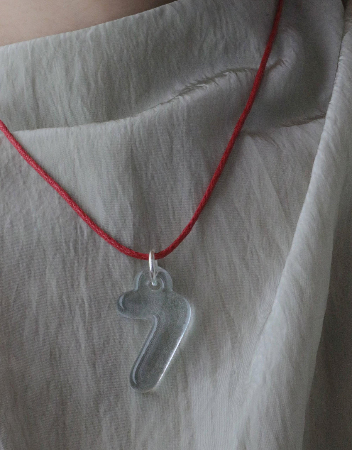 Red cotton cord necklace with adjustable length featuring a transparent number 7 charm pendant. Versatile accessory for layering or standalone wear. Ideal for pairing with additional charms. Eco-friendly waxed finish. Cord Necklace by CLED.
