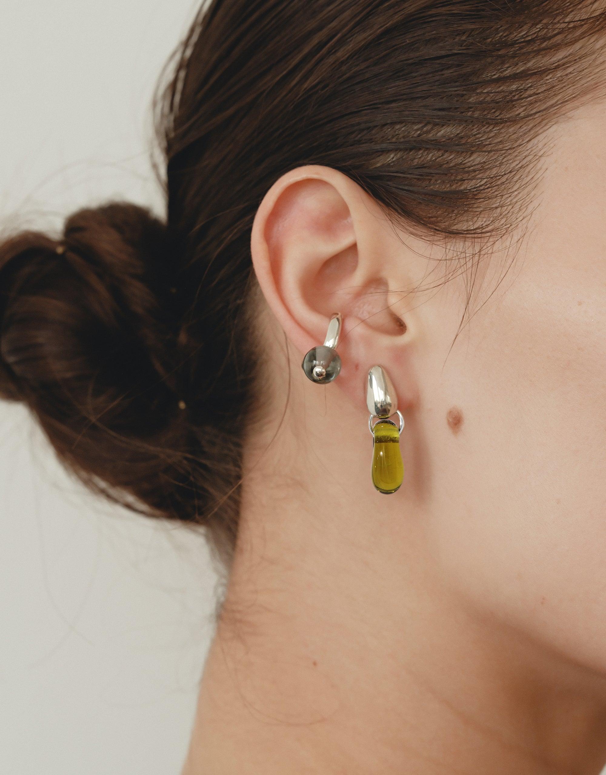Elegant Drop Counts Earrings featuring silver oval posts and vibrant yellow eco-friendly glass drops, showcasing minimalist design and sustainable craftsmanship. Worn by a model with dark hair in a bun, emphasizing the earrings' delicate raindrop-inspired aesthetic. Handmade jewelry by CLED.