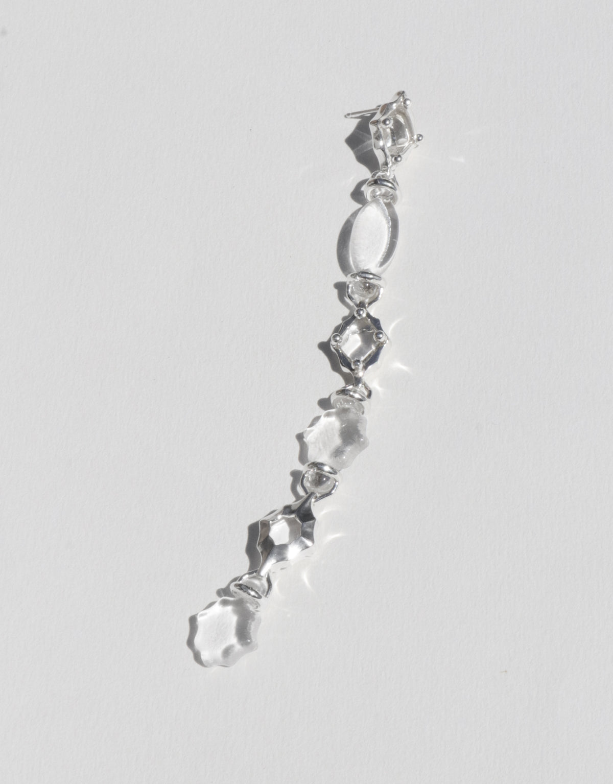 Cadence Linear Earring with clear glass Eco Gems descending in graduating sizes along a sterling silver line, each form linked to the next. A long single drop of upcycled glass handmade in Los Angeles. Cadence Linear Earring by CLED.