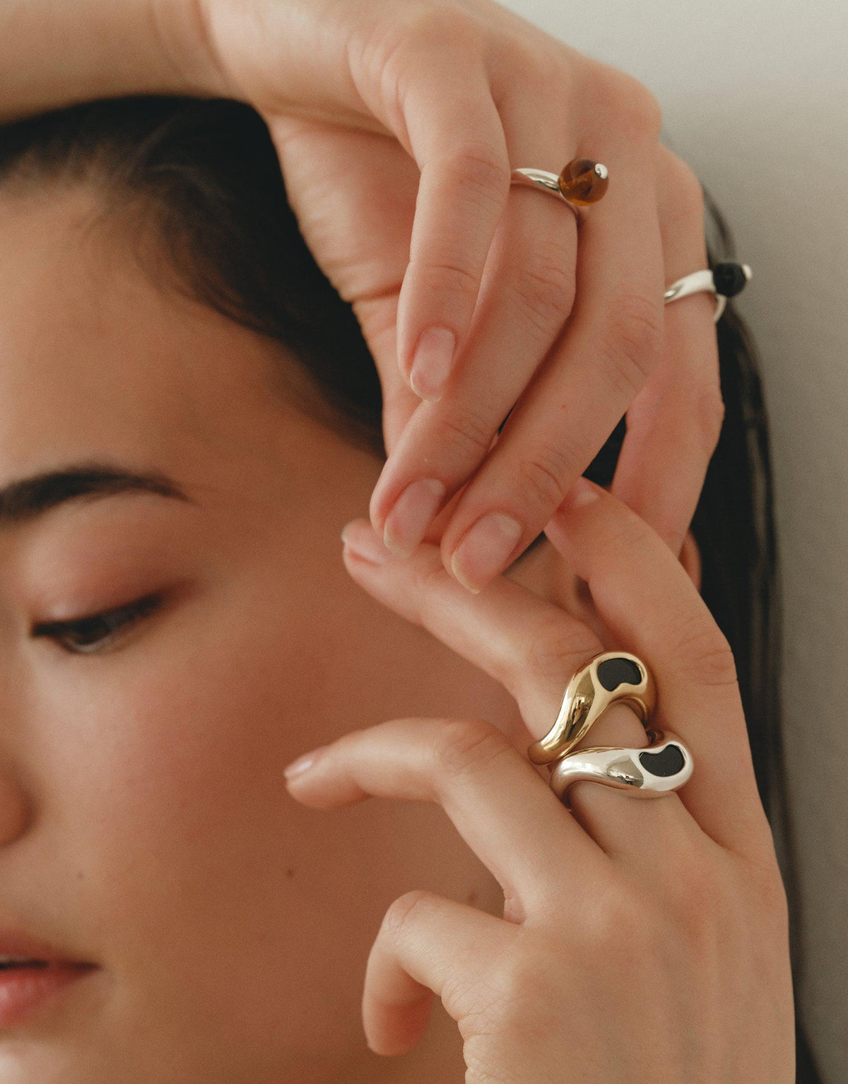 Close-up of hands wearing delicate rings, including a unique gold-toned Pea Curve Ring with organic shapes inspired by nature's creativity. The ring's design captures the essence of growth and transformation, reflecting the beauty of legume patterns. Pea Curve Ring | Small by CLED