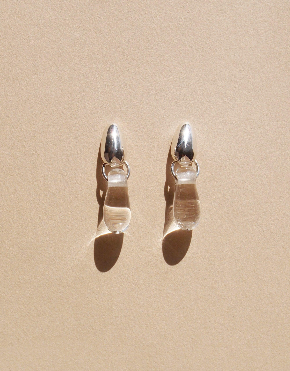 Elegant Drop Counts Earrings featuring oval silver posts and transparent teardrop-shaped pendants, inspired by water droplets. Handcrafted eco-friendly jewelry made from upcycled glass, showcasing minimalist design and sustainable craftsmanship. CLED