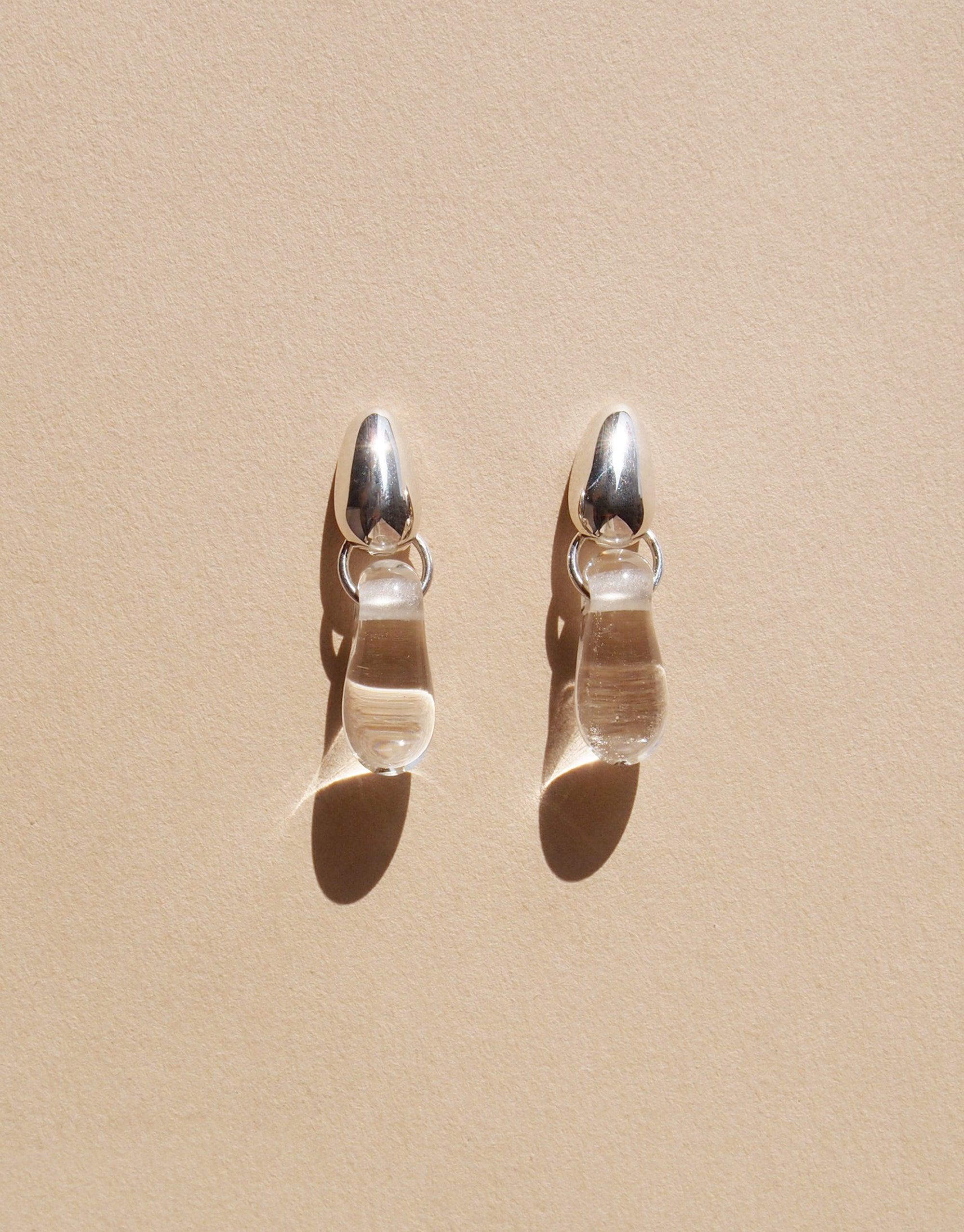 Elegant Drop Counts Earrings featuring oval silver posts and transparent teardrop-shaped pendants, inspired by water droplets. Handcrafted eco-friendly jewelry made from upcycled glass, showcasing minimalist design and sustainable craftsmanship. CLED