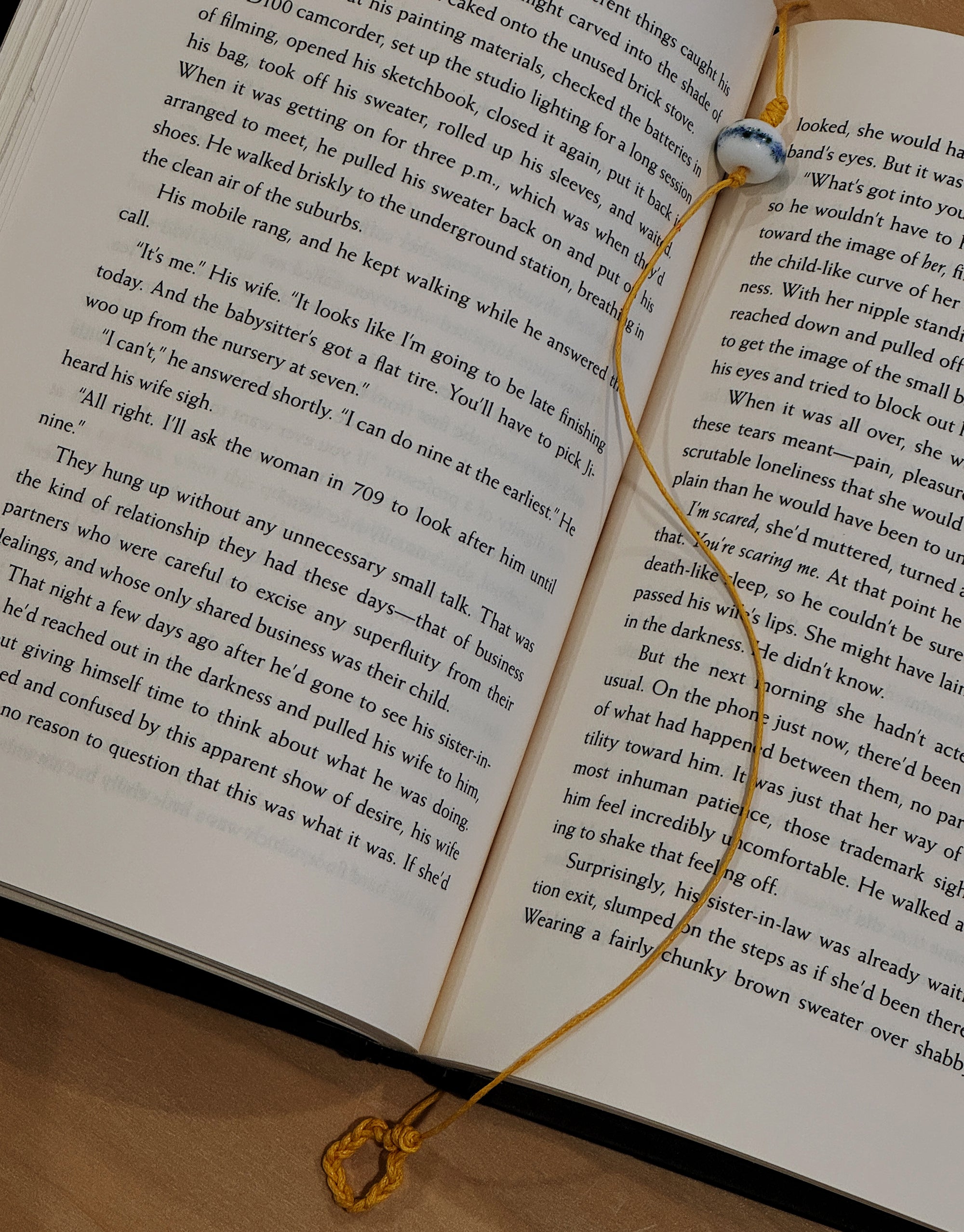 A book resting on a surface, adorned with a yellow cord and a shimmering blue and green splatter pattern glass bead.