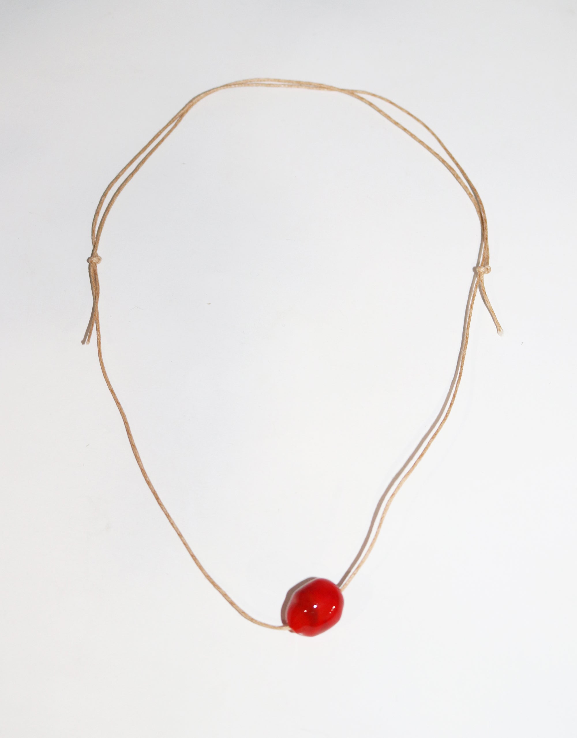 A simple necklace featuring a single red bead elegantly suspended on a delicate string. 
