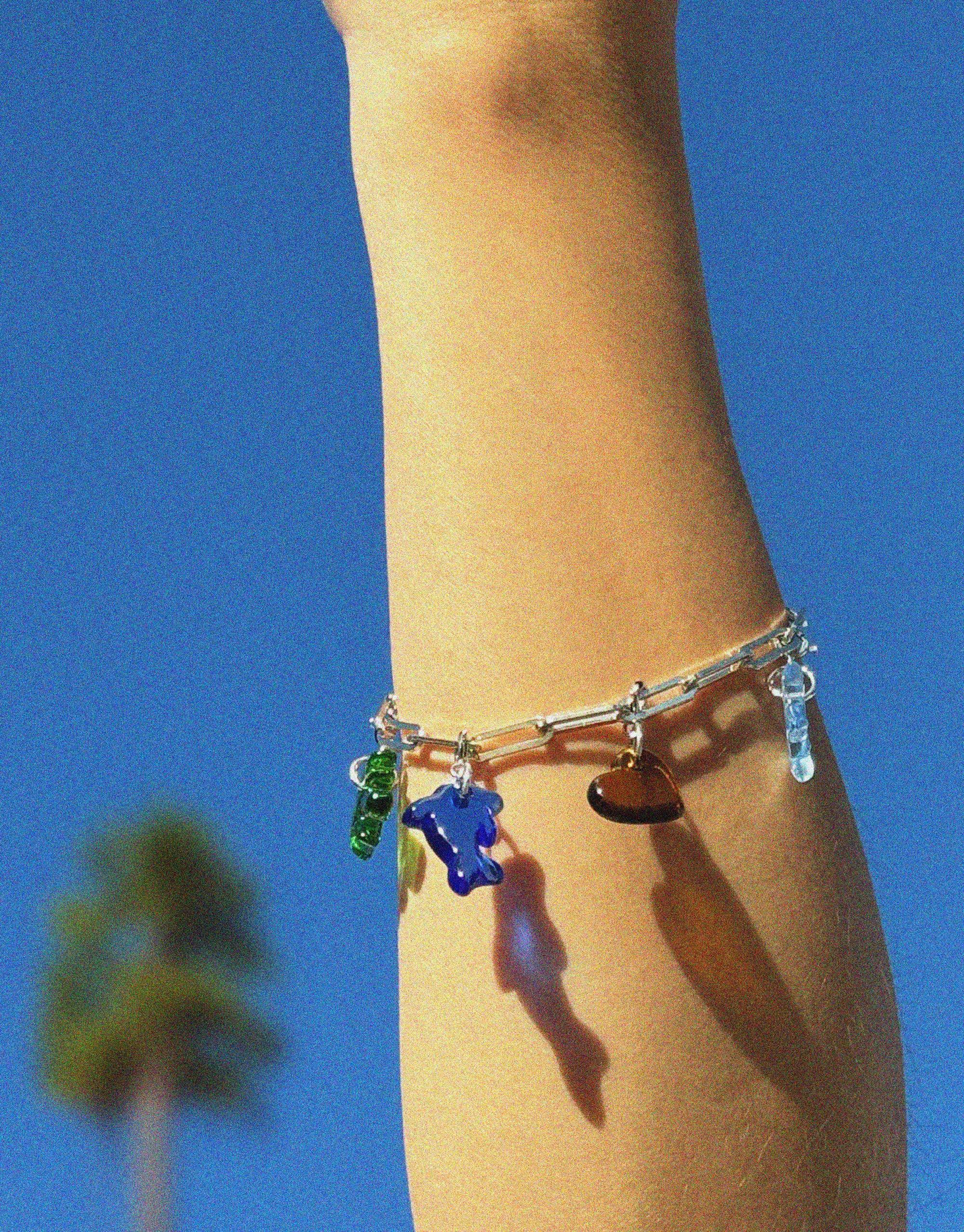 Stylish Icon Chain Bracelet with colorful charms on a wrist against a vibrant blue sky background. Versatile accessory for customizable looks. Icon Chain Bracelet | D by CLED
