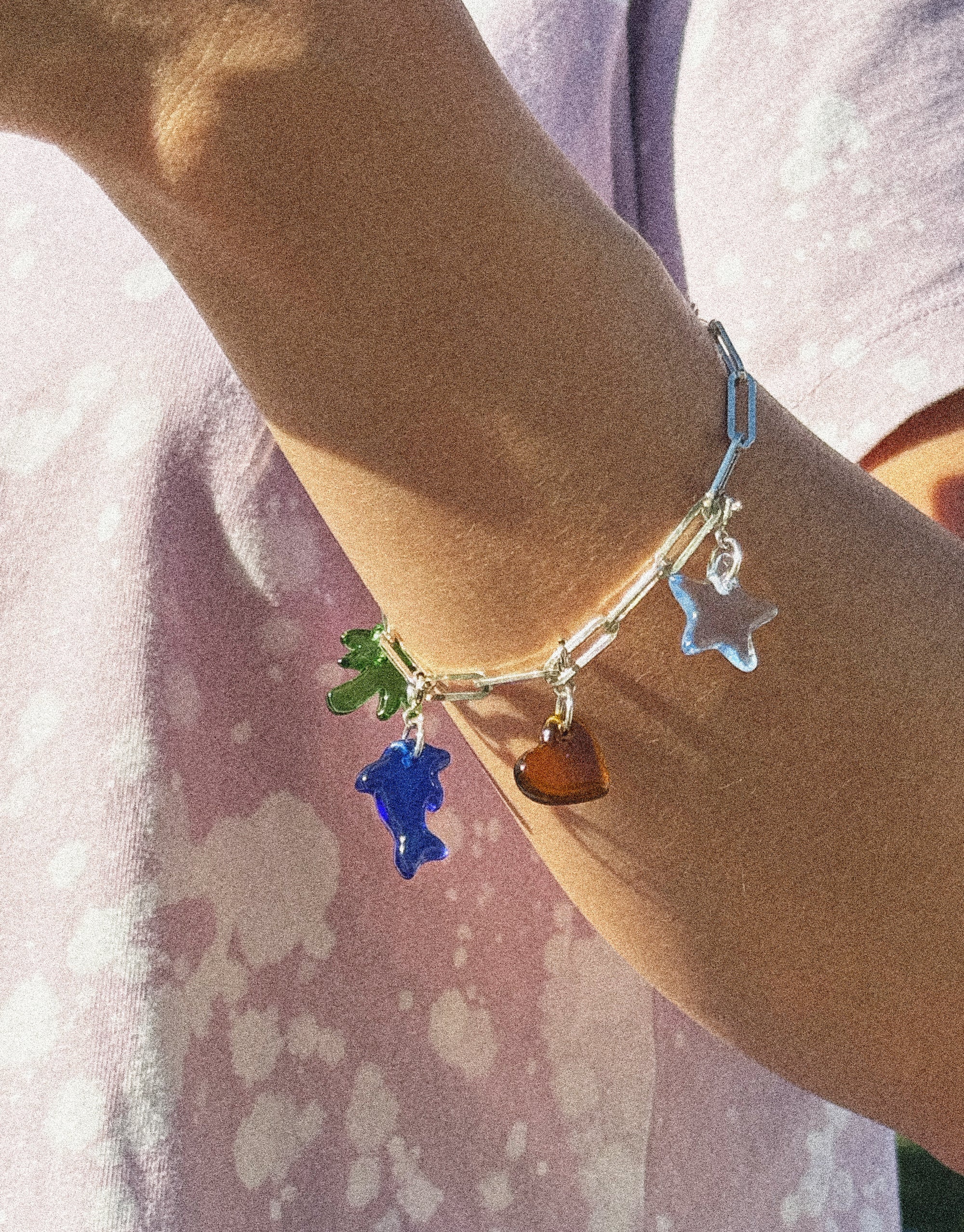 Close-up of a wrist wearing the Icon Chain Bracelet featuring colorful charms including a blue ghost, green leaf, orange heart, and silver star. Customizable jewelry piece for creating unique styles. Icon Chain Bracelet | D by CLED