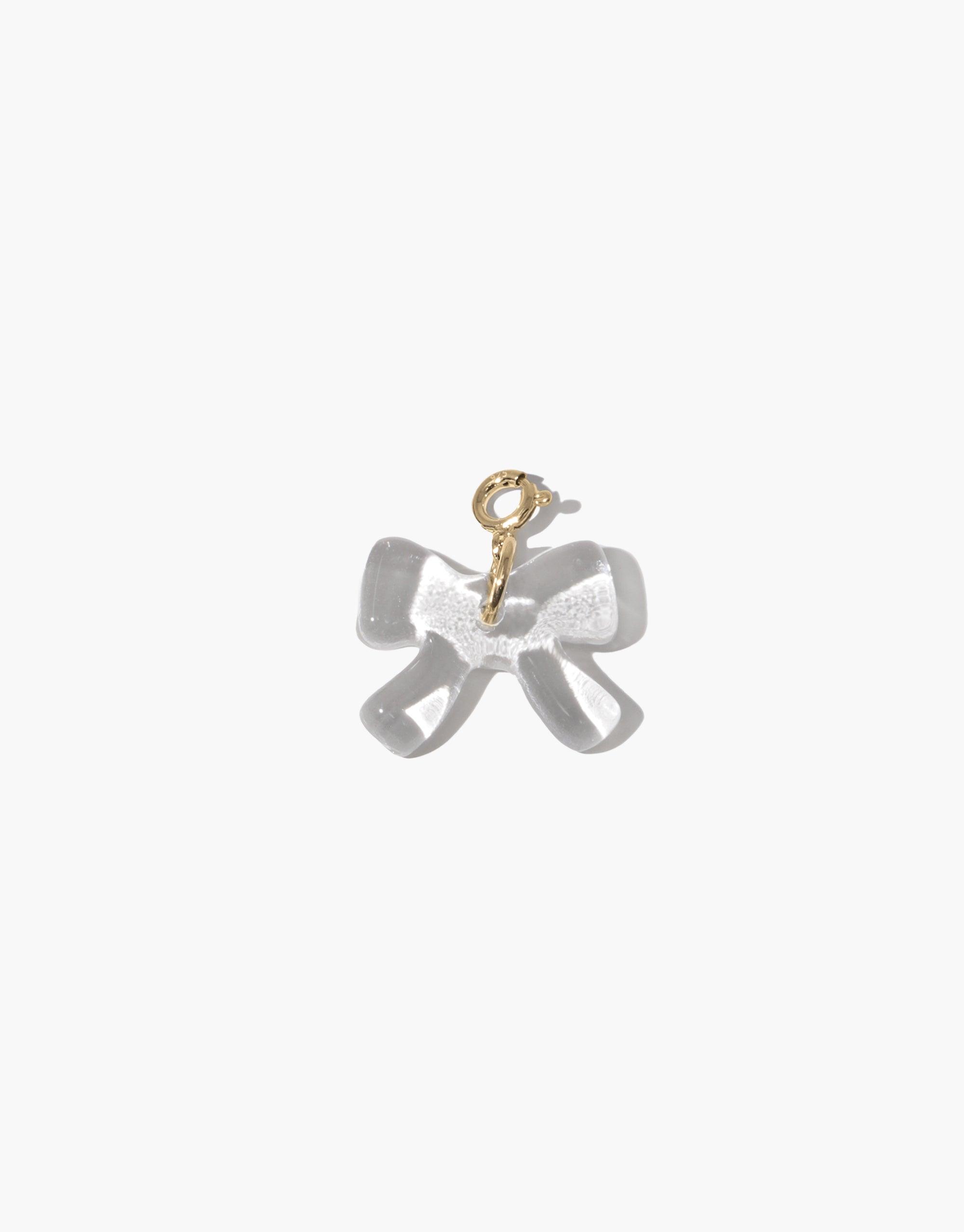 Elegant transparent bow-shaped charm with gold attachment loop, part of the Icon Charms collection. Playful and distinctive accessory for necklaces or bracelets. Bow A Icon Charm by CLED