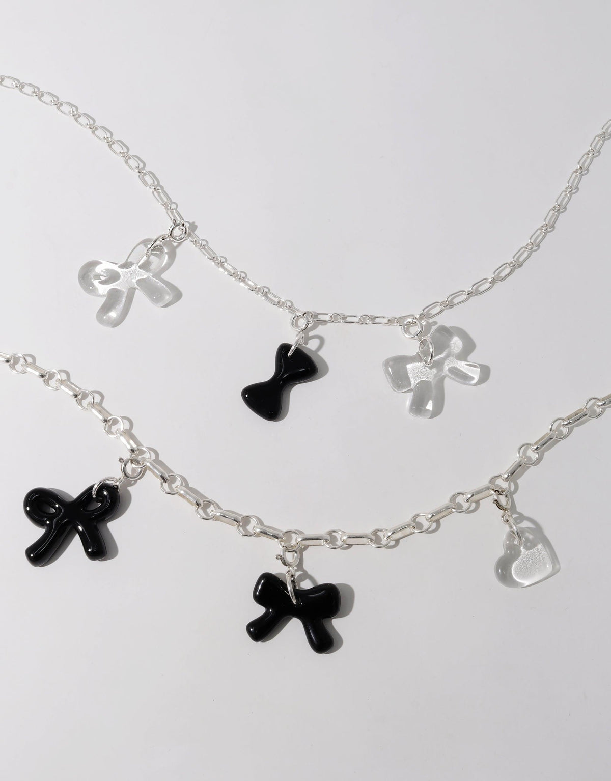 Delicate silver chain necklaces featuring charming bow-shaped pendants in black and clear, perfect for layering or wearing solo. Playful and versatile Icon Charm accessories to enhance any outfit. Bow B Icon Charm by CLED.