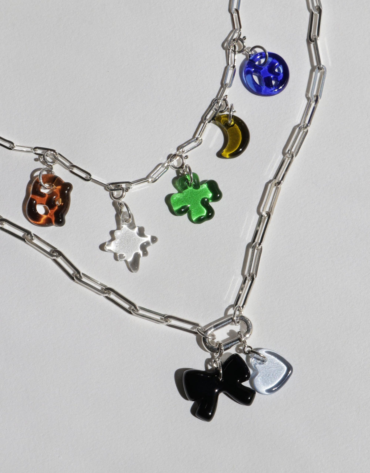 Silver chain necklace with colorful glass charms including blue sphere, green clover, orange cube, and black bow. Layered design for customizable styling. Icon Chain Necklace | E by CLED