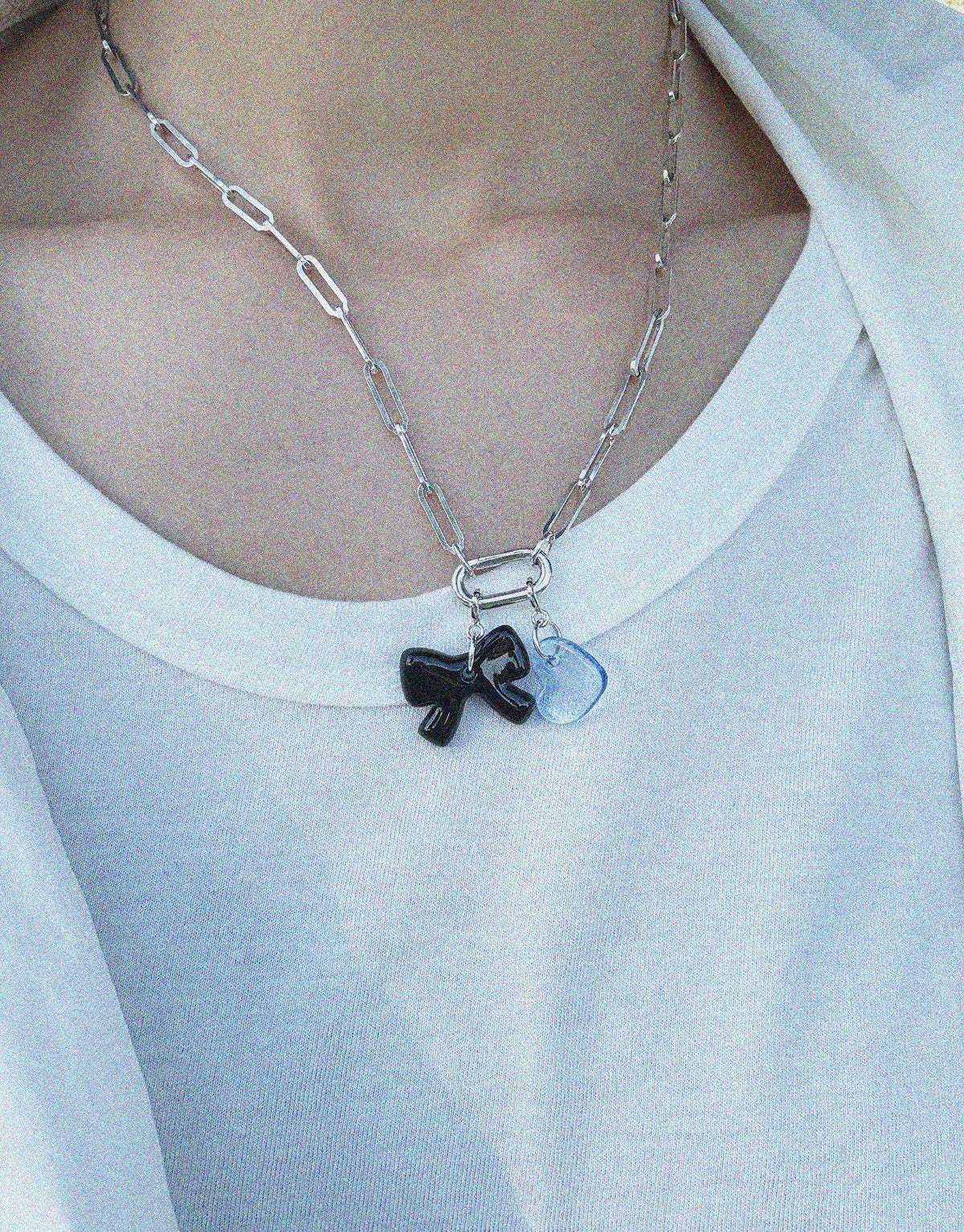 Silver chain necklace with black bow and blue charm pendants, worn on white top. Versatile Icon Chain Necklace | D for customizable style. Create a bold statement with interchangeable charms or wear alone. CLED