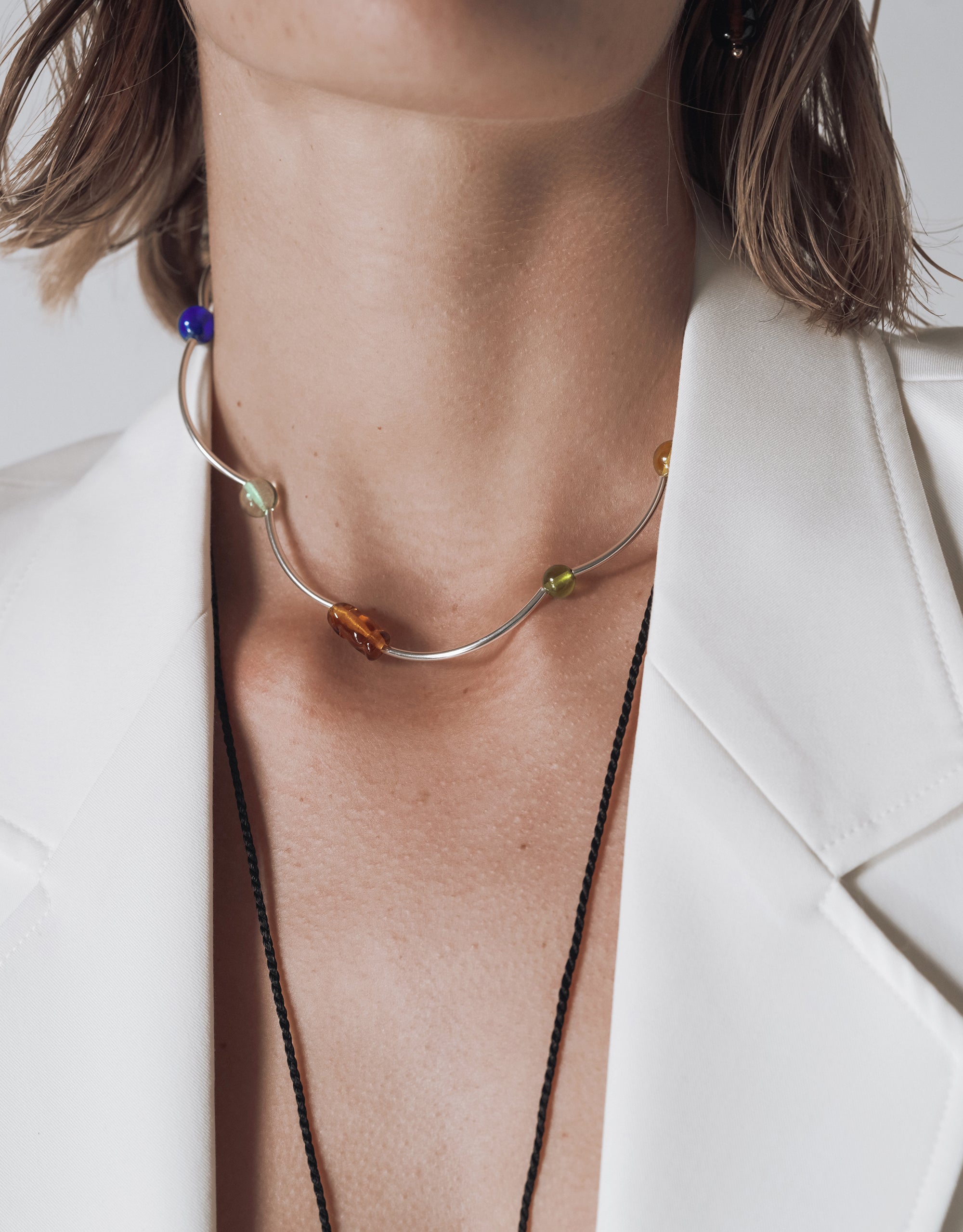 Halo Necklace with curved silver wire and colorful glass beads creating a flowing wave design against white blazer - CLED