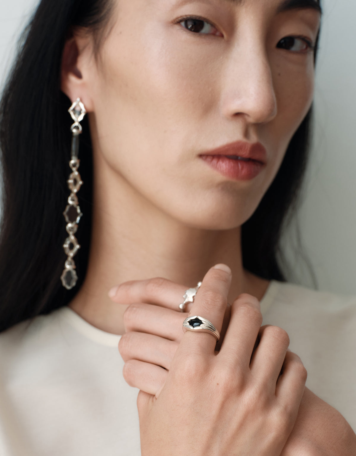 Cadence Linear Earring in clear glass worn with a black basalt signet ring, a long single drop of graduating upcycled glass Eco Gems in sterling silver. Cadence Linear Earring by CLED.