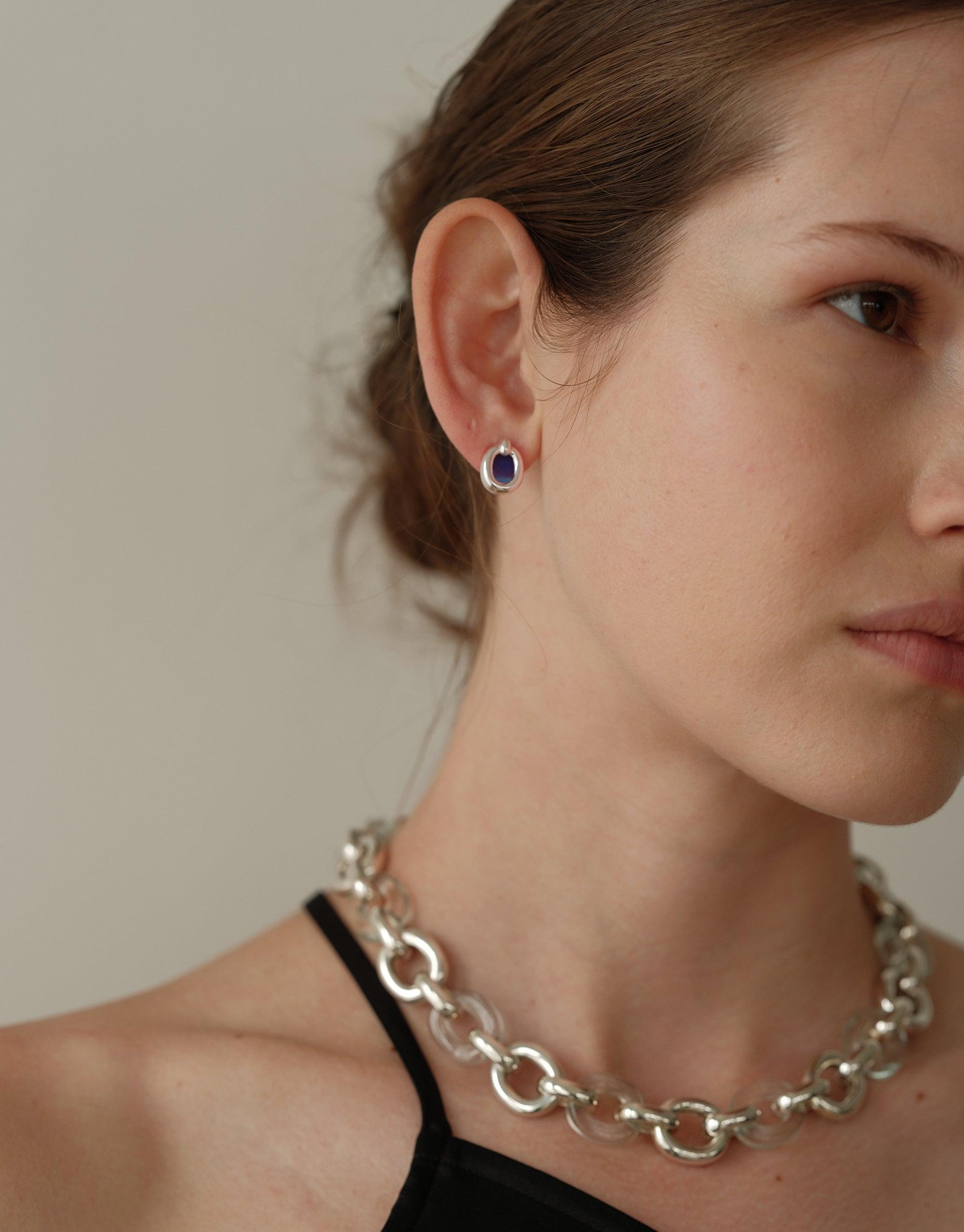 Close-up of a person wearing small circular earrings with a purple center, part of the Core Loop Earrings collection. The image also showcases a chunky silver chain necklace, highlighting the brand's upcycled jewelry style. Core Loop Earrings | Small by CLED.