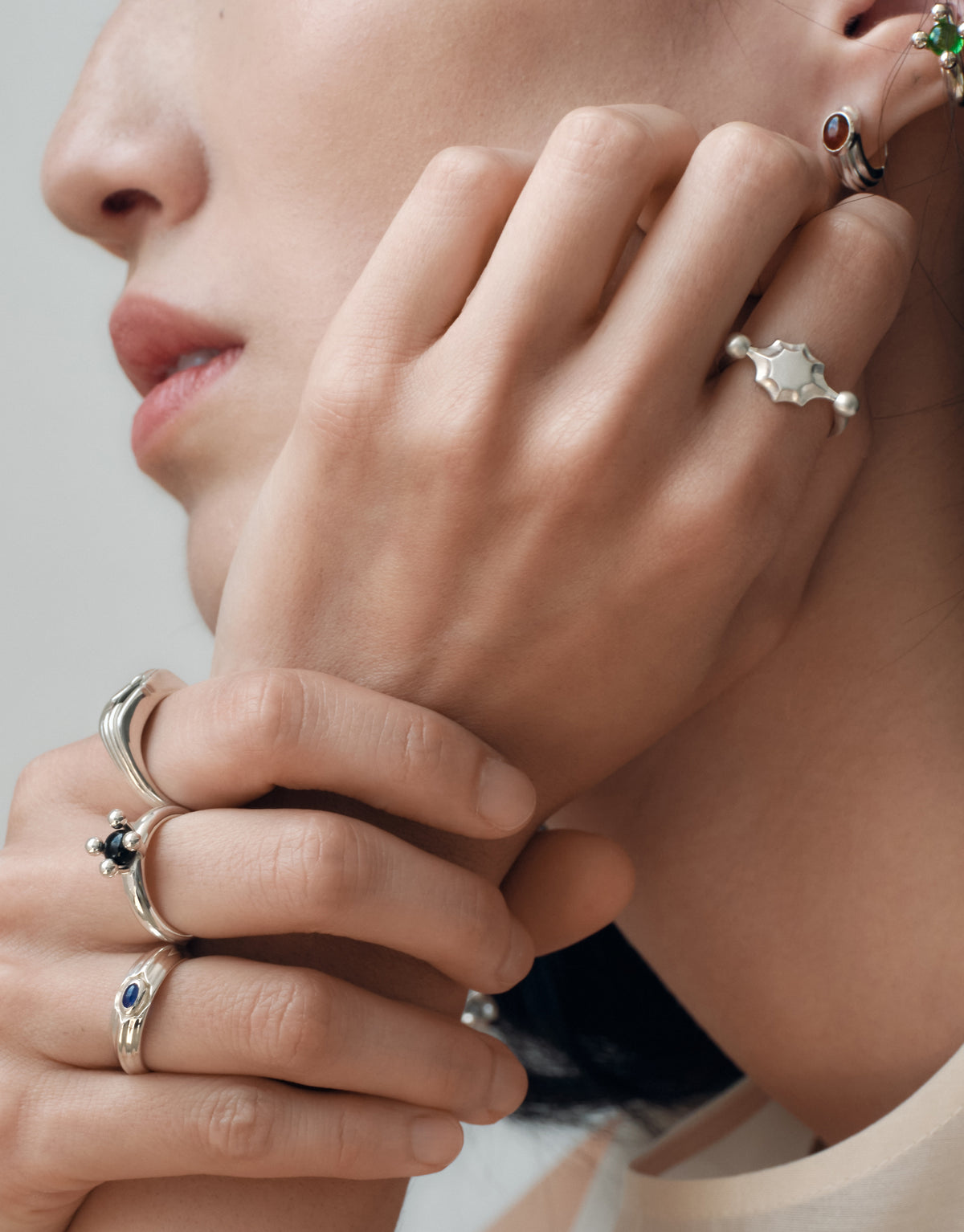 Eyelet Scallop Ring worn on the model, a hand raised to the chin with stacked sterling silver rings. Handmade in Los Angeles. Eyelet Scallop Ring by CLED.