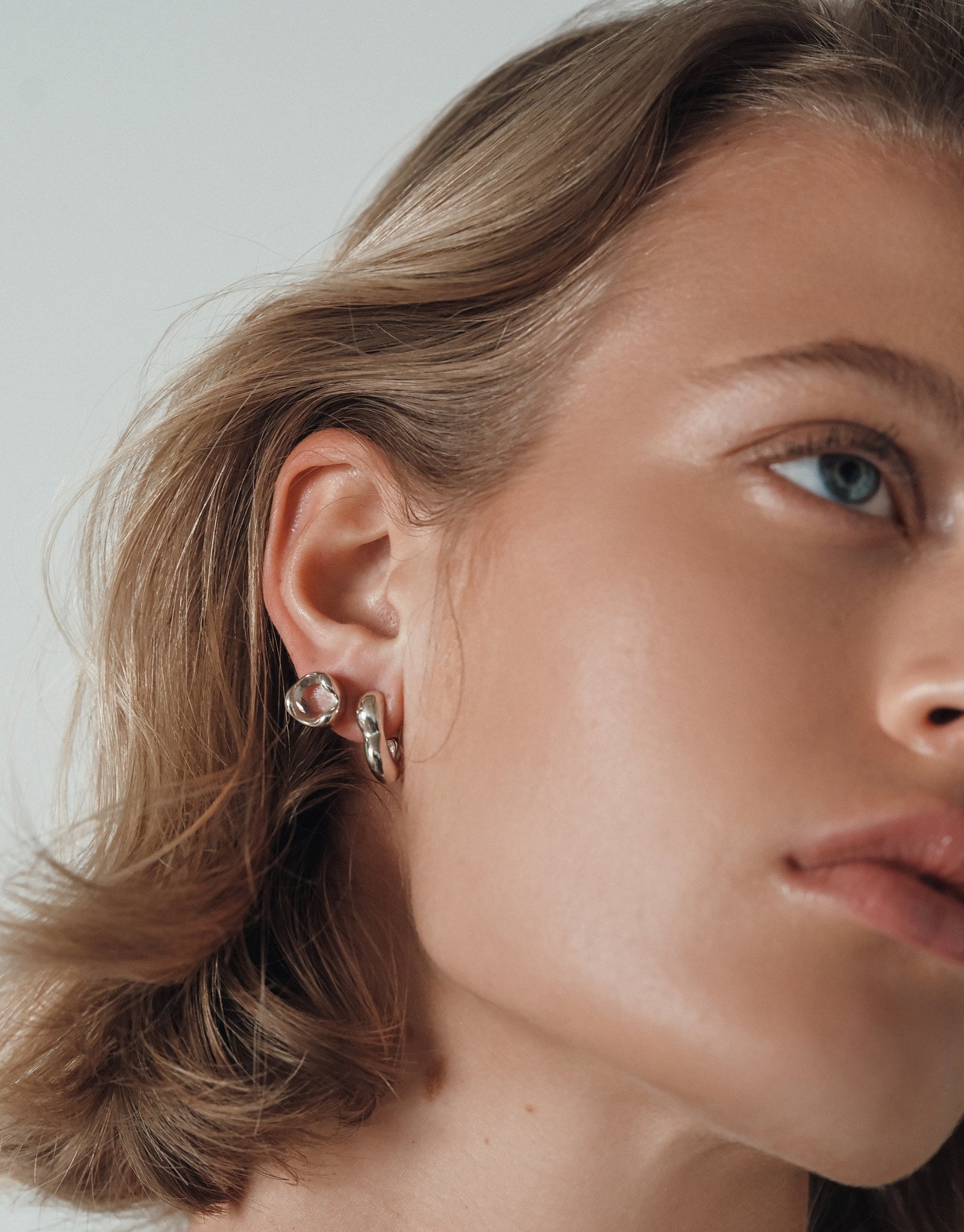 Close-up of Orb Stud Earrings with curved silver bezel and clear eco-friendly cabochon, shown on ear against minimal background - CLED