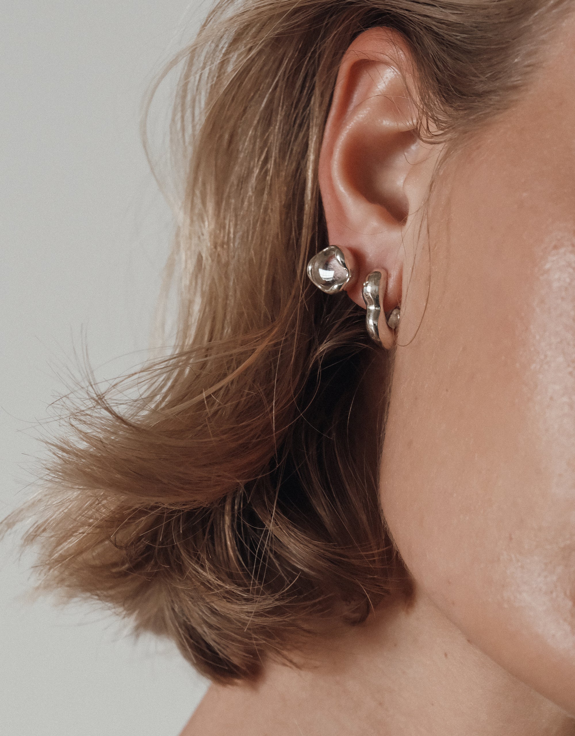 Flow Hoop Earrings with sculptural curved design shown on ear, featuring elegant undulating silver waves - by CLED