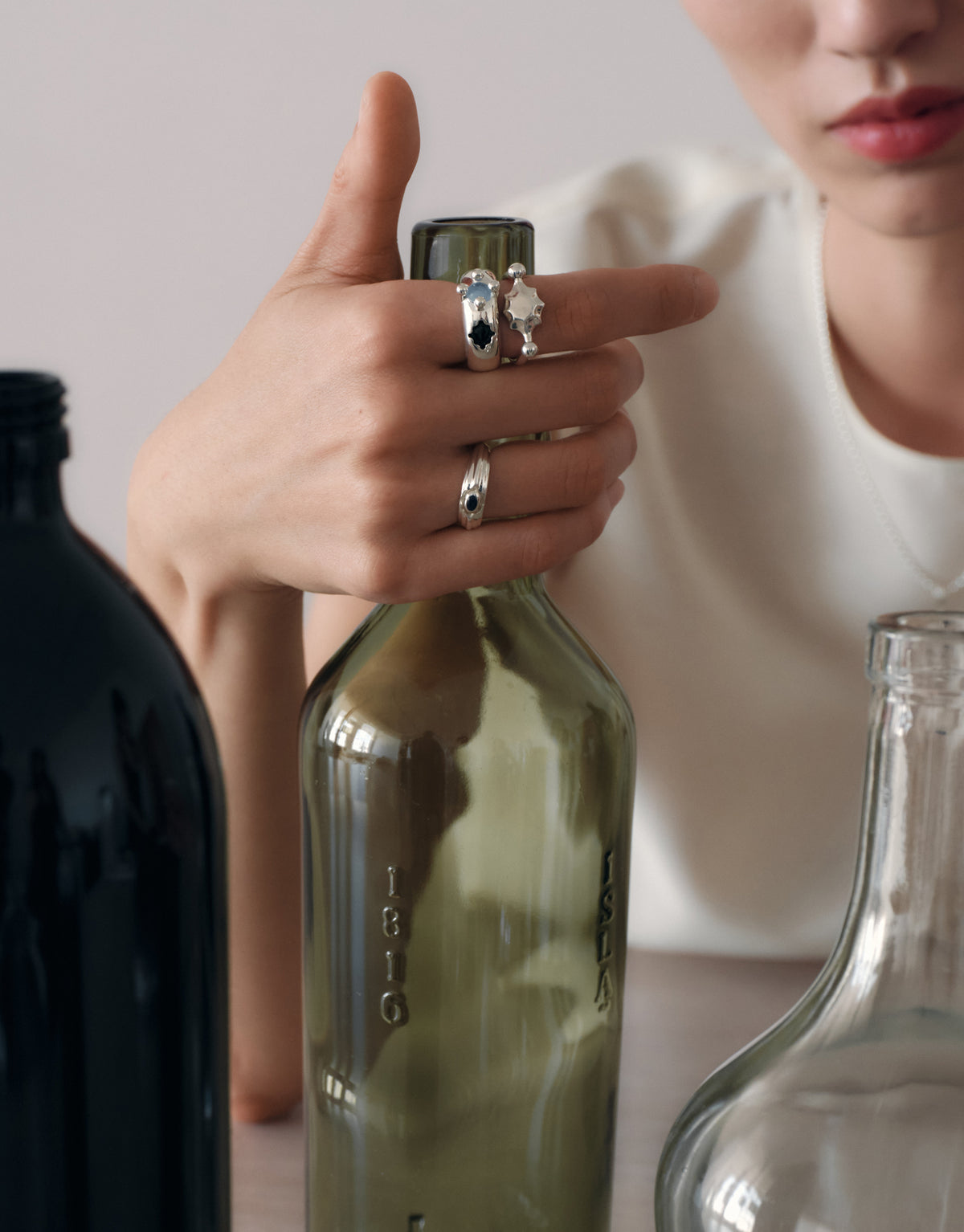 Eyelet Scallop Ring worn on the model, a hand resting on discarded glass bottles, the source of every CLED Eco Gem. Handmade in Los Angeles. Eyelet Scallop Ring by CLED.
