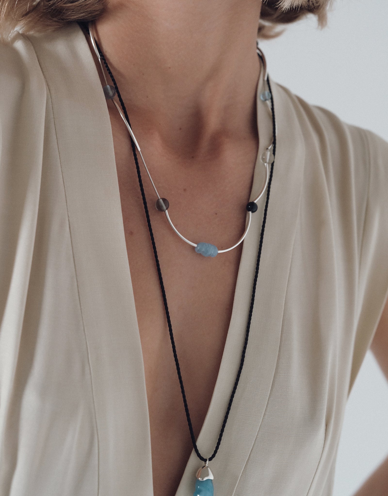 Halo Necklace featuring curved silver bars and blue glass beads on delicate chain, styled with ivory robe by CLED
