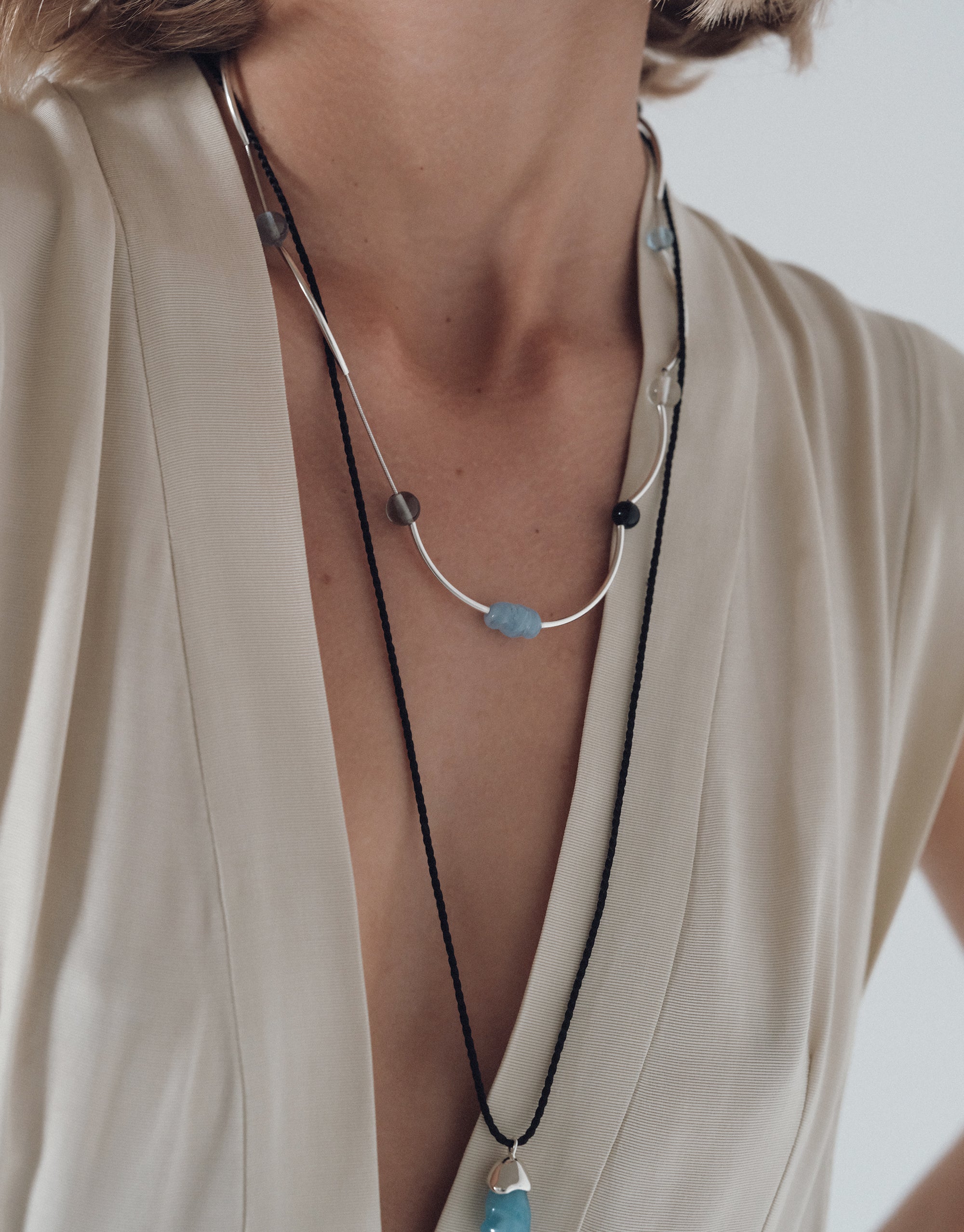 Halo Necklace featuring curved silver bars and blue glass beads on delicate chain, styled with ivory robe by CLED