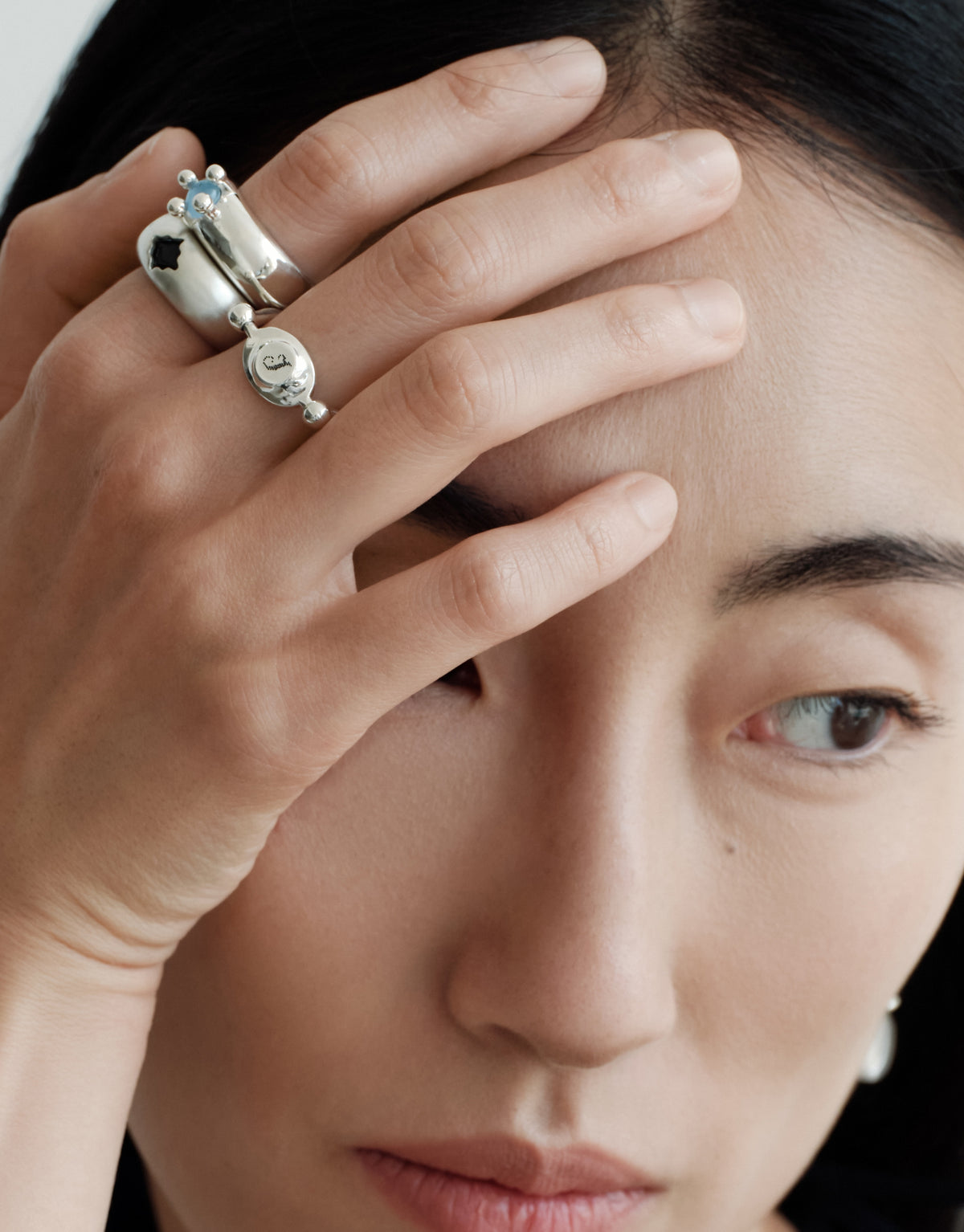 LAS Oval Swivel Ring | Metal worn on the model, a hand raised to the face with sterling silver rings. Handmade in Los Angeles. LAS Oval Swivel Ring | Metal by CLED.