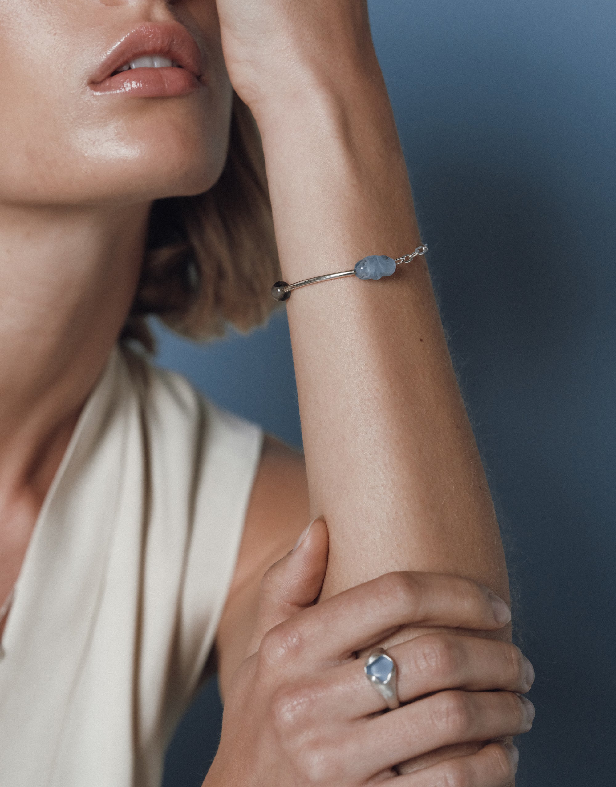 Elegant close-up of a woman's lips and wrist, highlighting a silver bracelet with blue and dark beads against soft lighting.