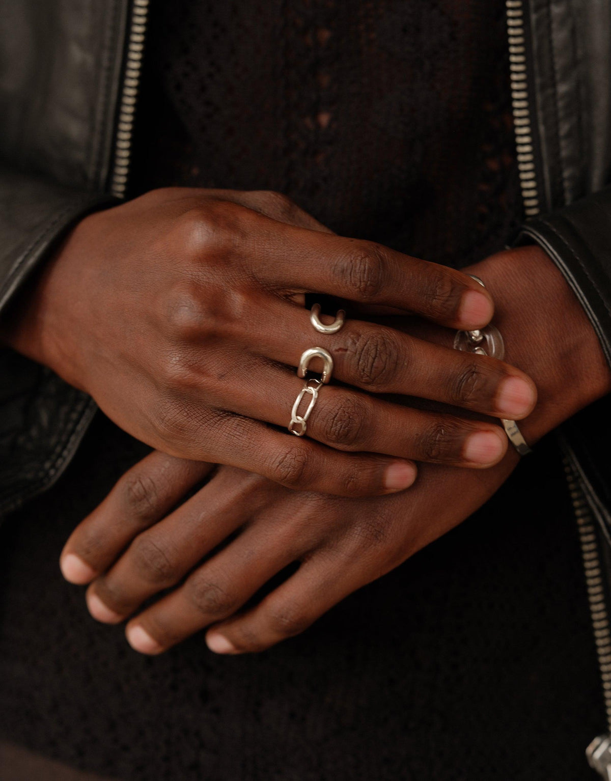 Close-up of hands wearing multiple silver rings, including the Infinite Loop Ring, showcasing unique designs against dark clothing. Symbolizes unity and connection in the Loop Collection. Sustainable jewelry by CLED.