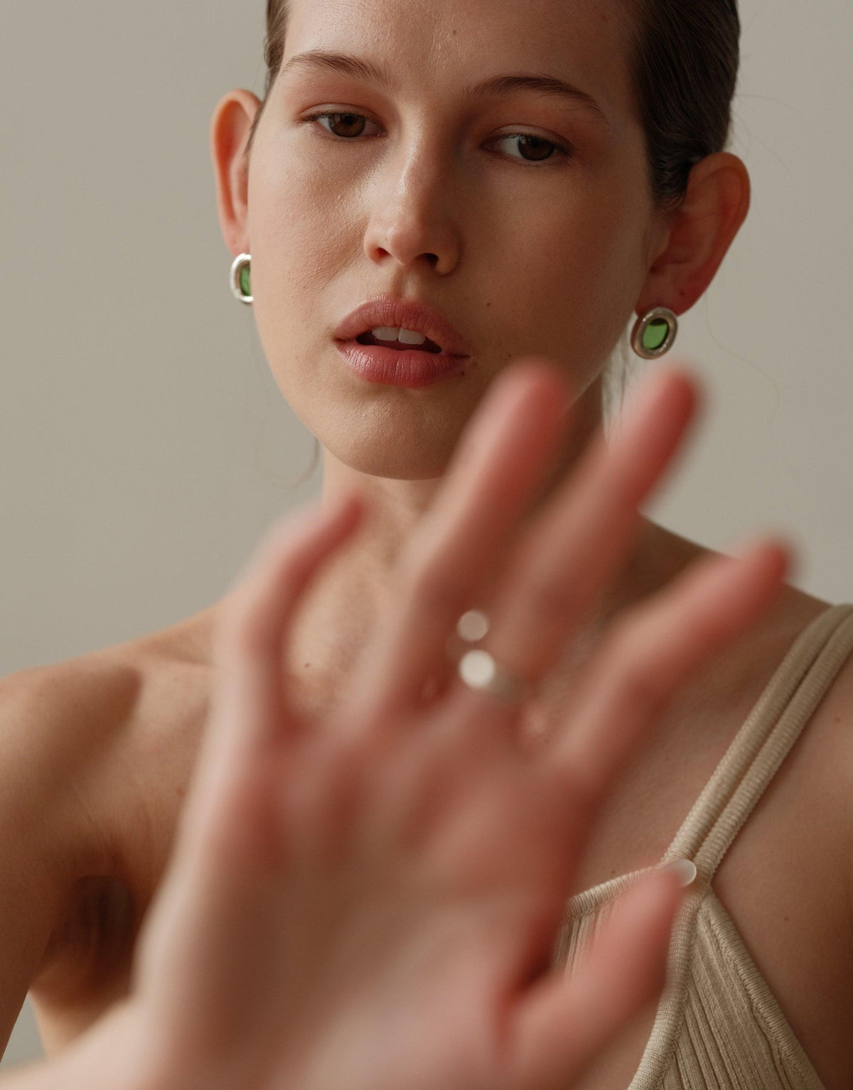Close-up of model wearing large circular green earrings, emphasizing sustainable jewelry design. Hand in foreground, showcasing additional rings. Soft, neutral tones highlight the Core Loop Earrings | Large, part of the upcycled collection by CLED.