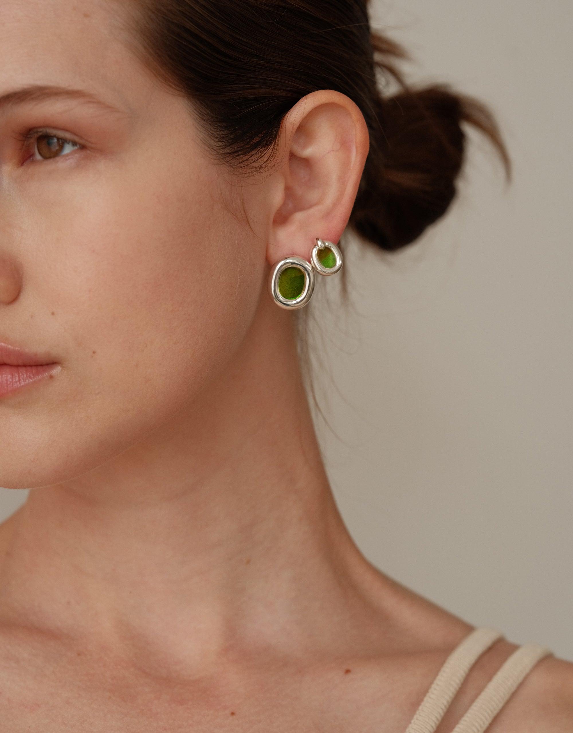 Close-up view of small circular earrings with green centers, showcasing the Core Loop Earrings | Small design. The earrings feature a sleek silver frame surrounding a vibrant green interior, highlighting the upcycled aesthetic and minimalist style of the CLED collection.