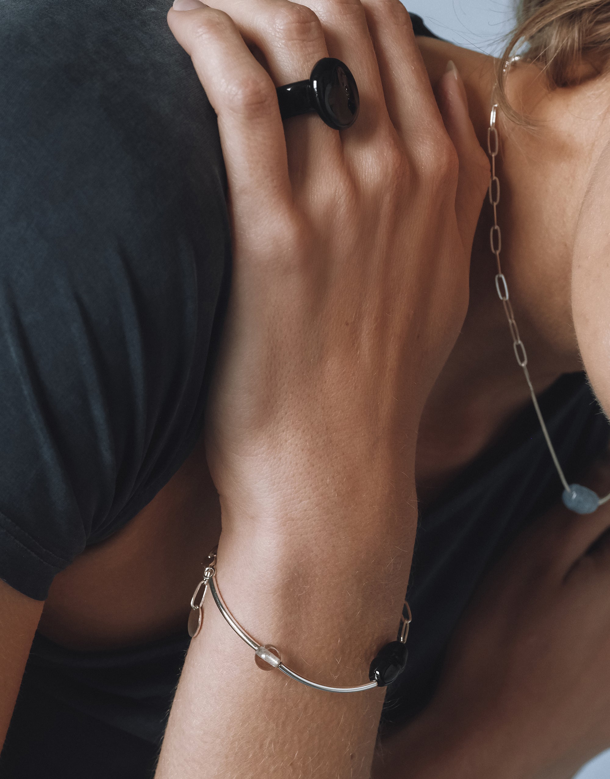 Close-up of a woman's hand adorned with a glossy black statement ring and a silver bracelet featuring a black Eco Gem and clear bead, paired with a delicate silver chain necklace.