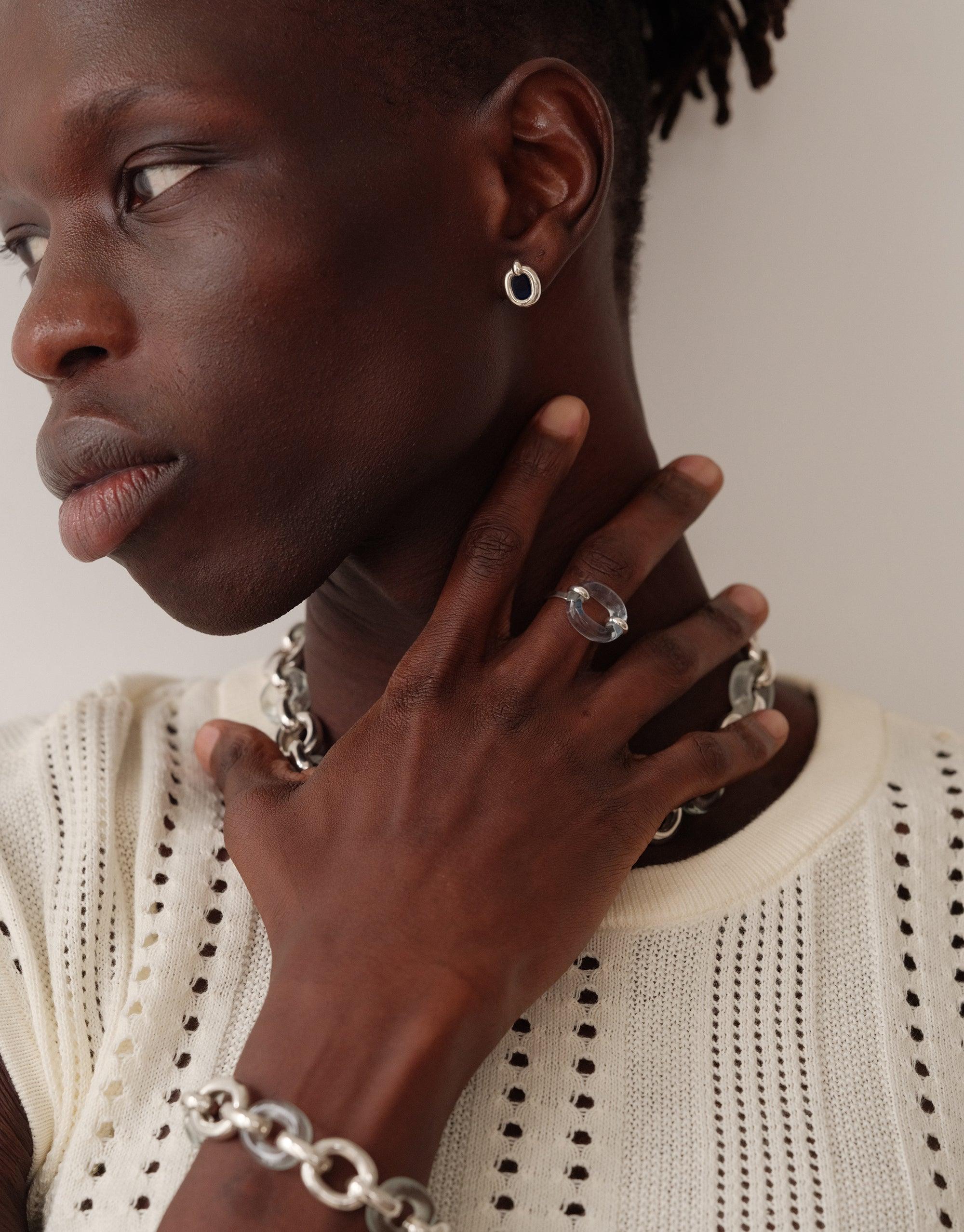 Close-up of a person wearing small silver loop earrings, rings, and chain jewelry, showcasing the Core Loop Earrings | Small. The model is wearing a white knit sweater, emphasizing the elegant contrast with the jewelry. Upcycled, sustainable fashion by CLED.