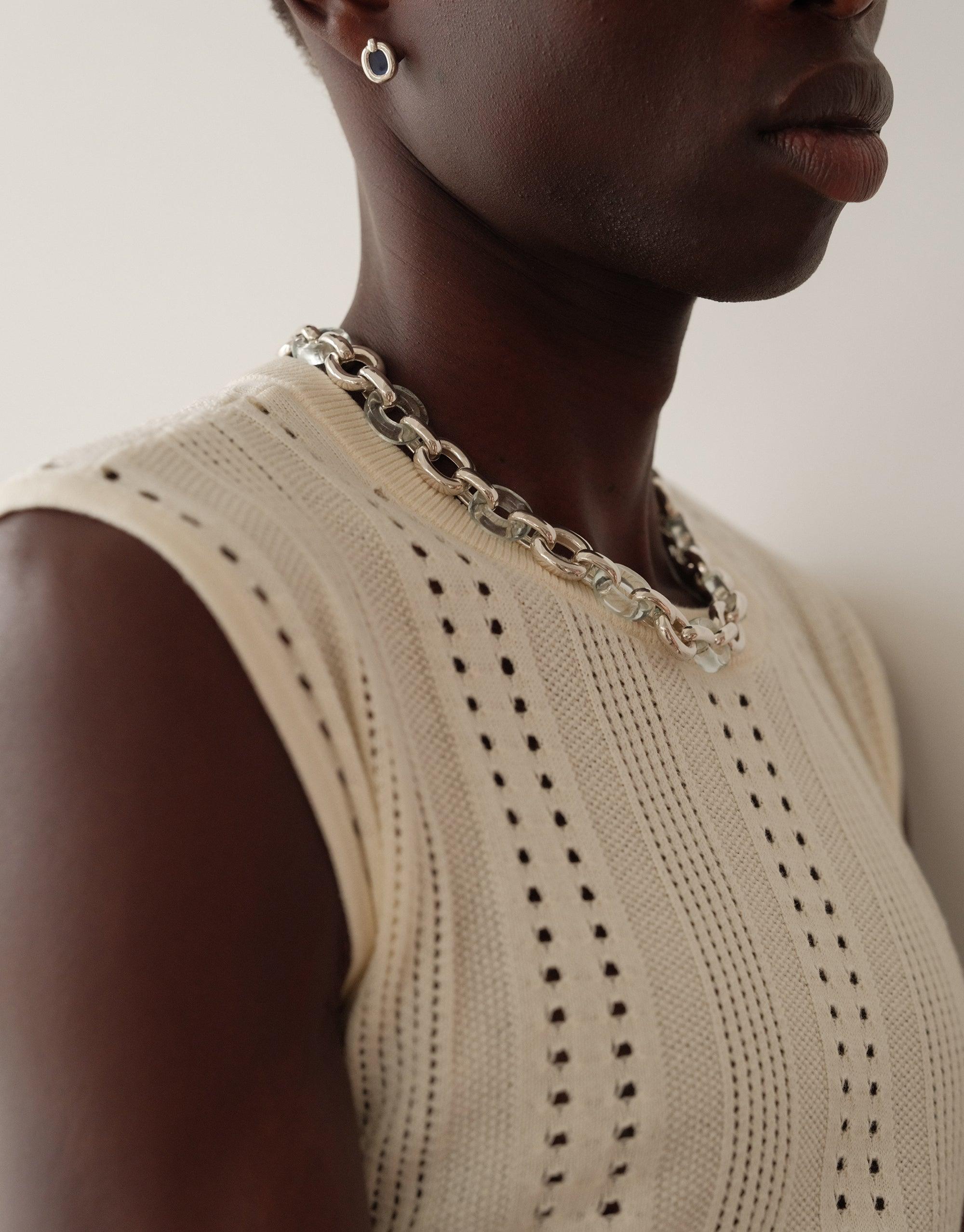 Close-up of a model wearing small circular earrings, showcasing the Core Loop Earrings | Small. The earrings complement a cream-colored knit top and chunky silver necklace, embodying unity and upcycled elegance. CLED