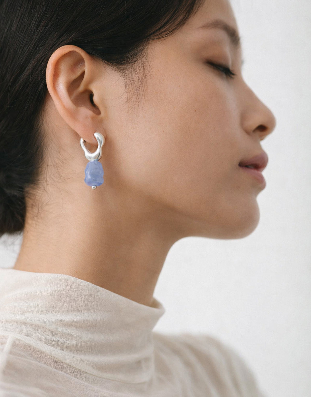 Close-up of a person wearing a silver earring with a blue gemstone on a plain background