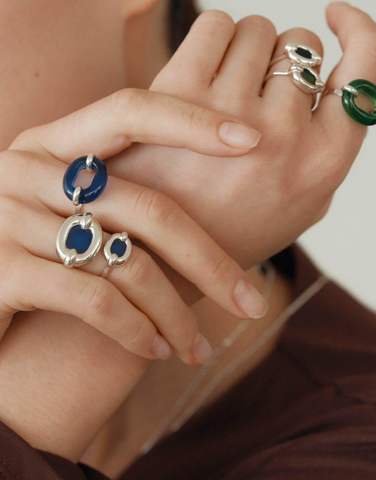 Close-up of hands wearing unique silver rings with blue and green circular elements, showcasing the In The Loop Ring design. Stylish and sustainable jewelry pieces by CLED.
