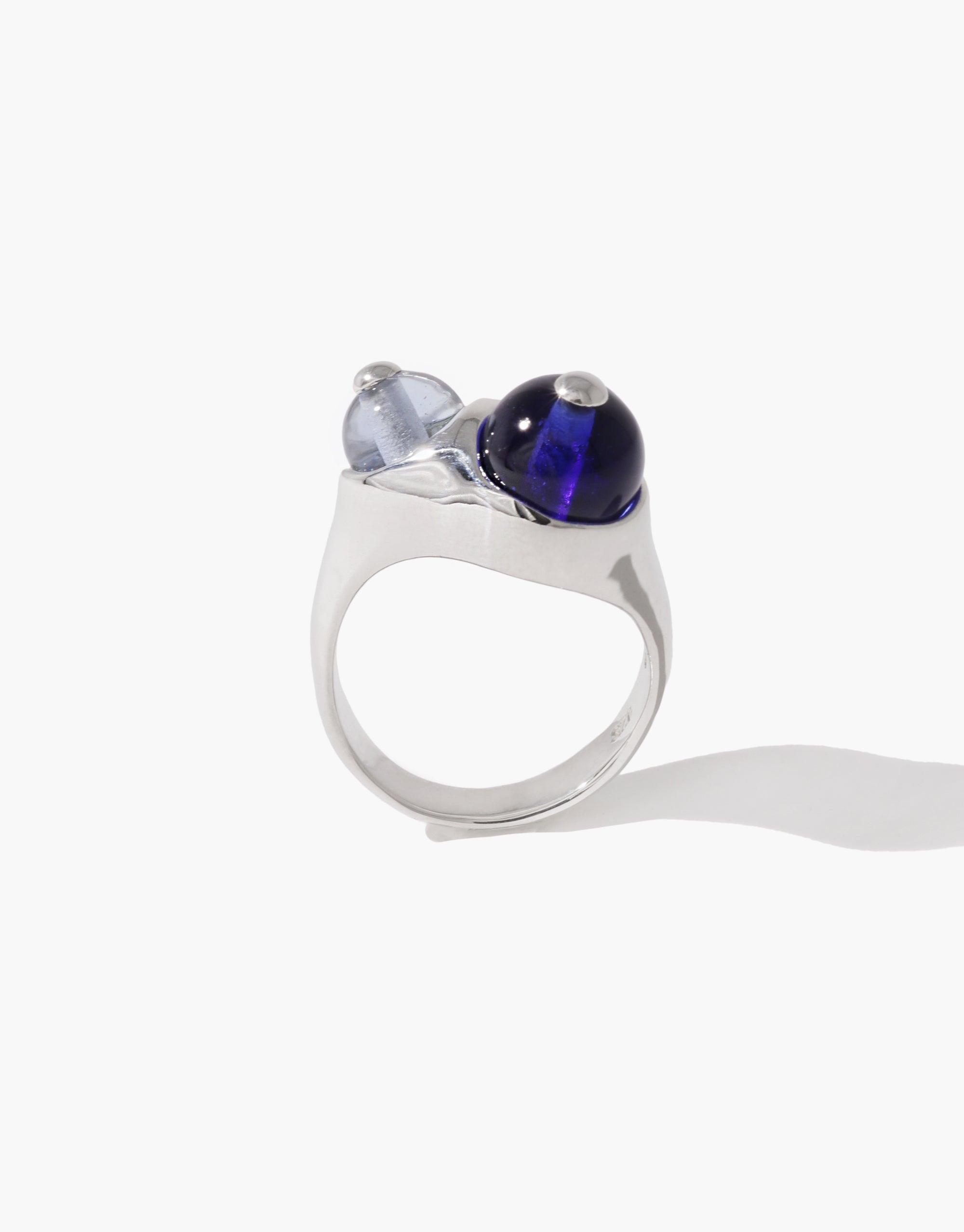 Silver Pod Ring featuring two spherical glass beads, one clear and one deep blue, set on a sleek modern band, inspired by organic legume shapes and natural growth patterns. Elegant and unique jewelry piece. CLED Pod Ring