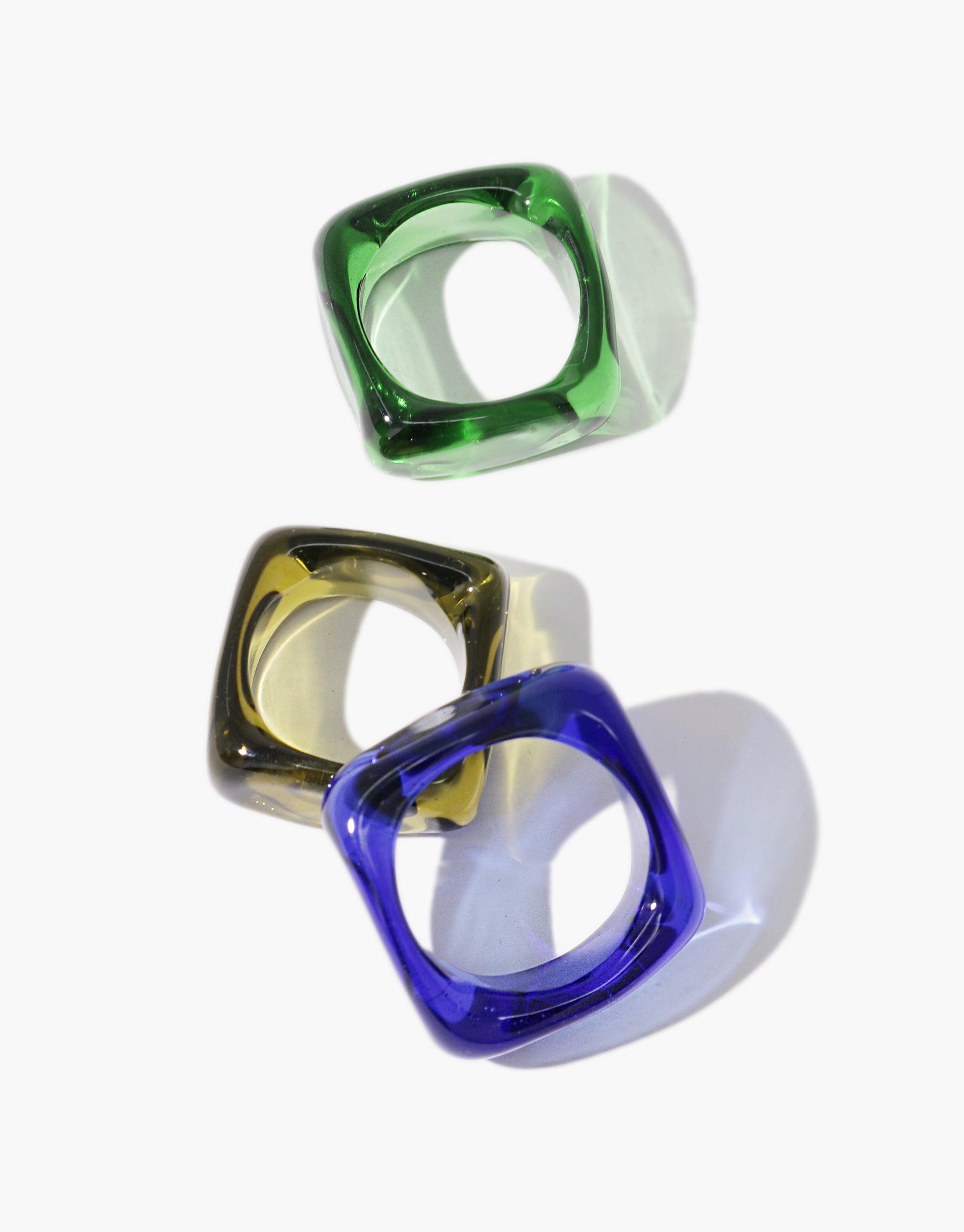 Three square-shaped glass rings in vibrant green, amber, and blue colors, showcasing unique translucent designs for the Engravable Dice Ring. These stylish accessories offer a modern, geometric aesthetic with customizable features. CLED