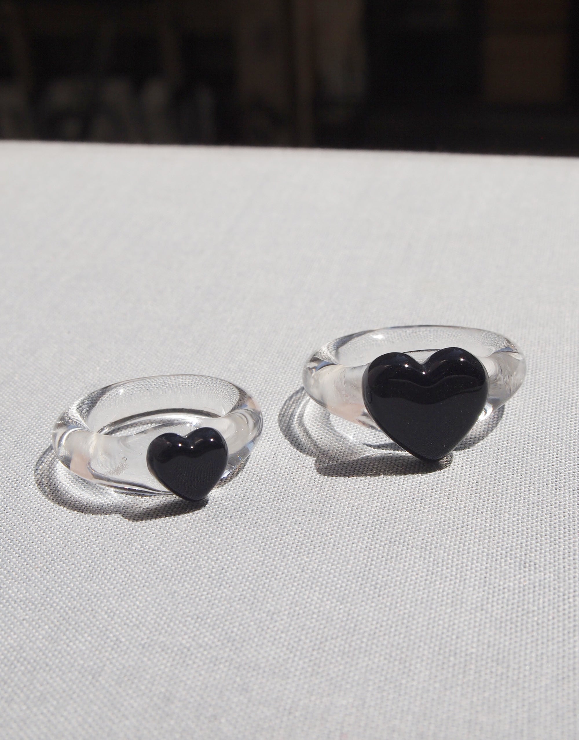 Two silver rings with black heart-shaped designs, one larger and one smaller, displayed on a light-colored fabric. Elegant and stylish Heart Icon Ring | Large, perfect for showcasing love and affection. CLED