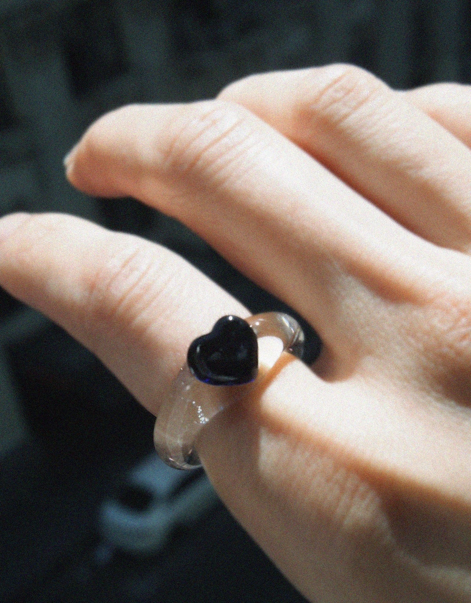 Close-up of a hand wearing a delicate ring featuring a small black heart-shaped icon on a translucent band. The Heart Icon Ring | Small showcases elegant simplicity and modern design, perfect for everyday wear. CLED