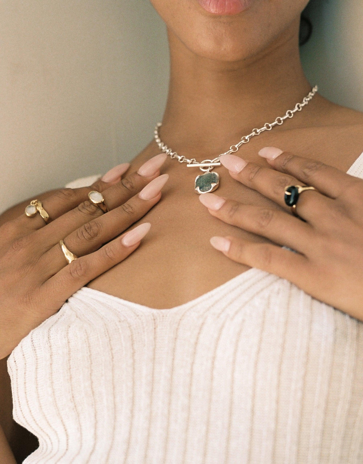 Close-up of hands wearing multiple rings, including the Oval Sculpture Ring, and a necklace with a green pendant. Showcases eco-friendly jewelry designs and upcycled materials. Oval Sculpture Ring by CLED