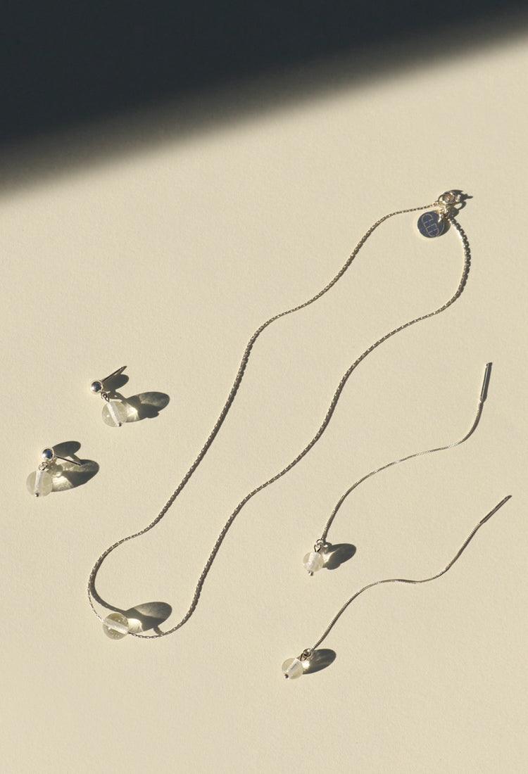Minimal Ball Necklace featuring a delicate silver chain with a transparent eco-friendly glass pendant. Accompanied by matching earrings and additional pendants, showcasing the versatility of this elegant jewelry set. Stylish and sustainable accessories by CLED.
