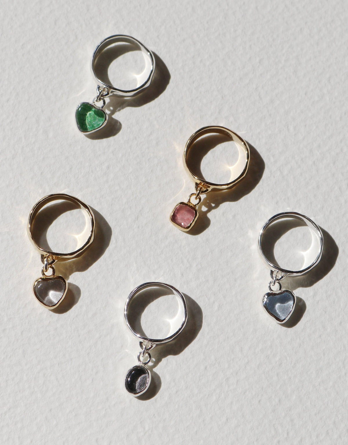 Oval Dangling Ring collection featuring five rings with colorful upcycled glass charms in heart and circular shapes, available in sterling silver and gold-plated brass. Handmade eco-friendly jewelry showcasing sustainability and style. CLED