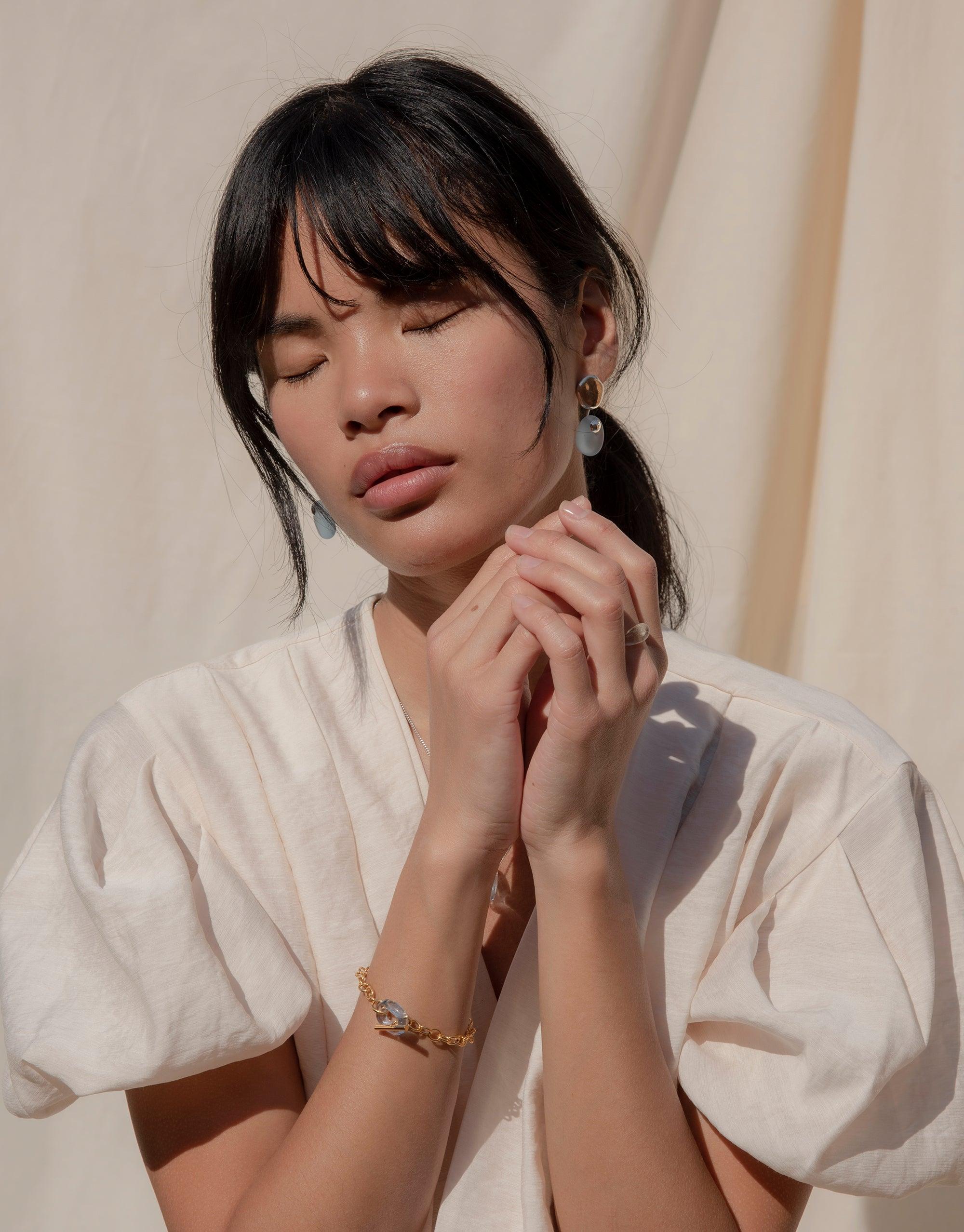 Woman wearing white top displaying ITL Toggle Bracelet with interlocking links and eco gem, highlighting delicate design and handcrafted quality of sustainable jewelry piece by CLED