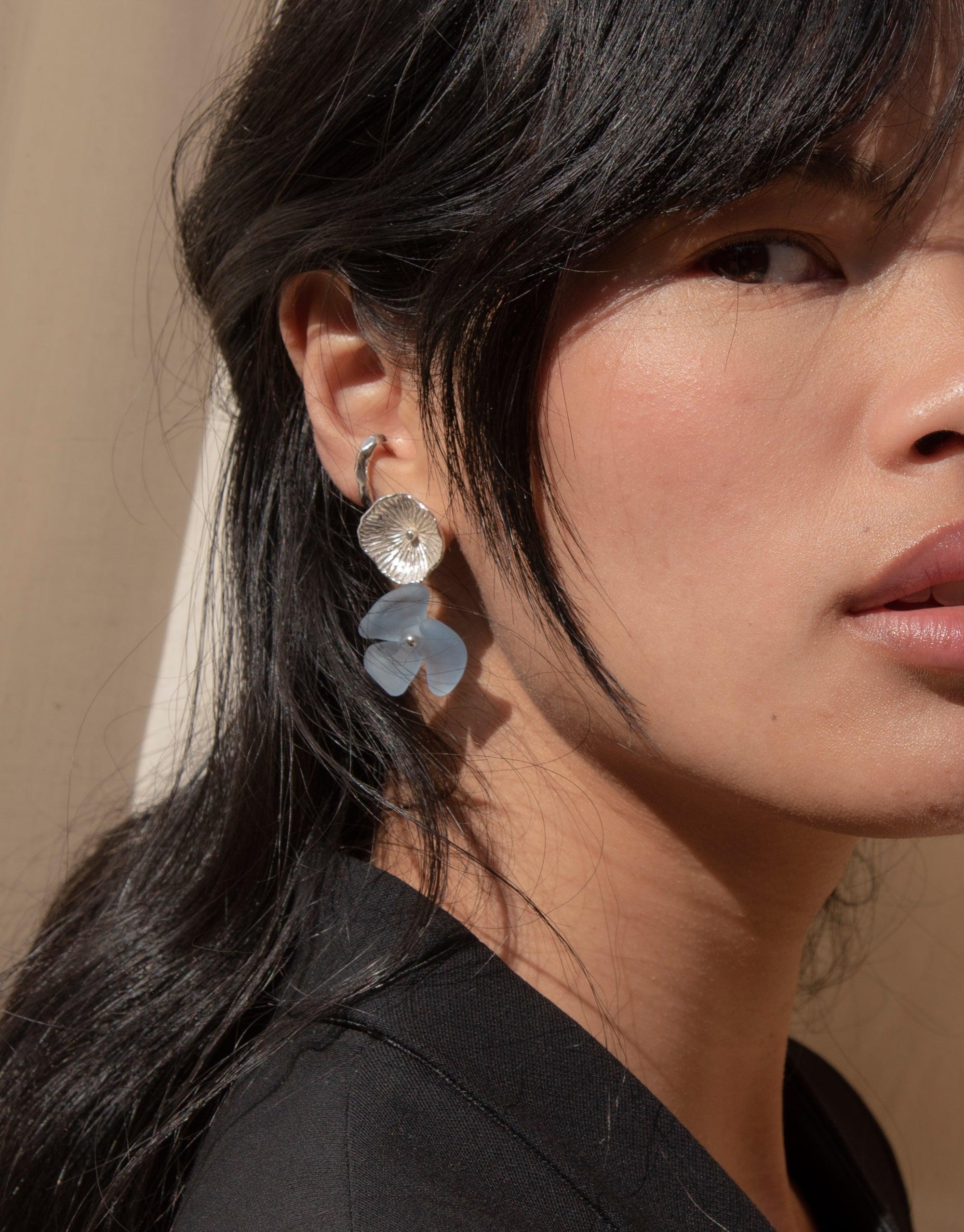 Close-up view of Periwinkle Single Earrings featuring a silver floral stud with a delicate blue glass petal drop, showcasing the eco-friendly design and handcrafted details. Elegant and sustainable jewelry by CLED.