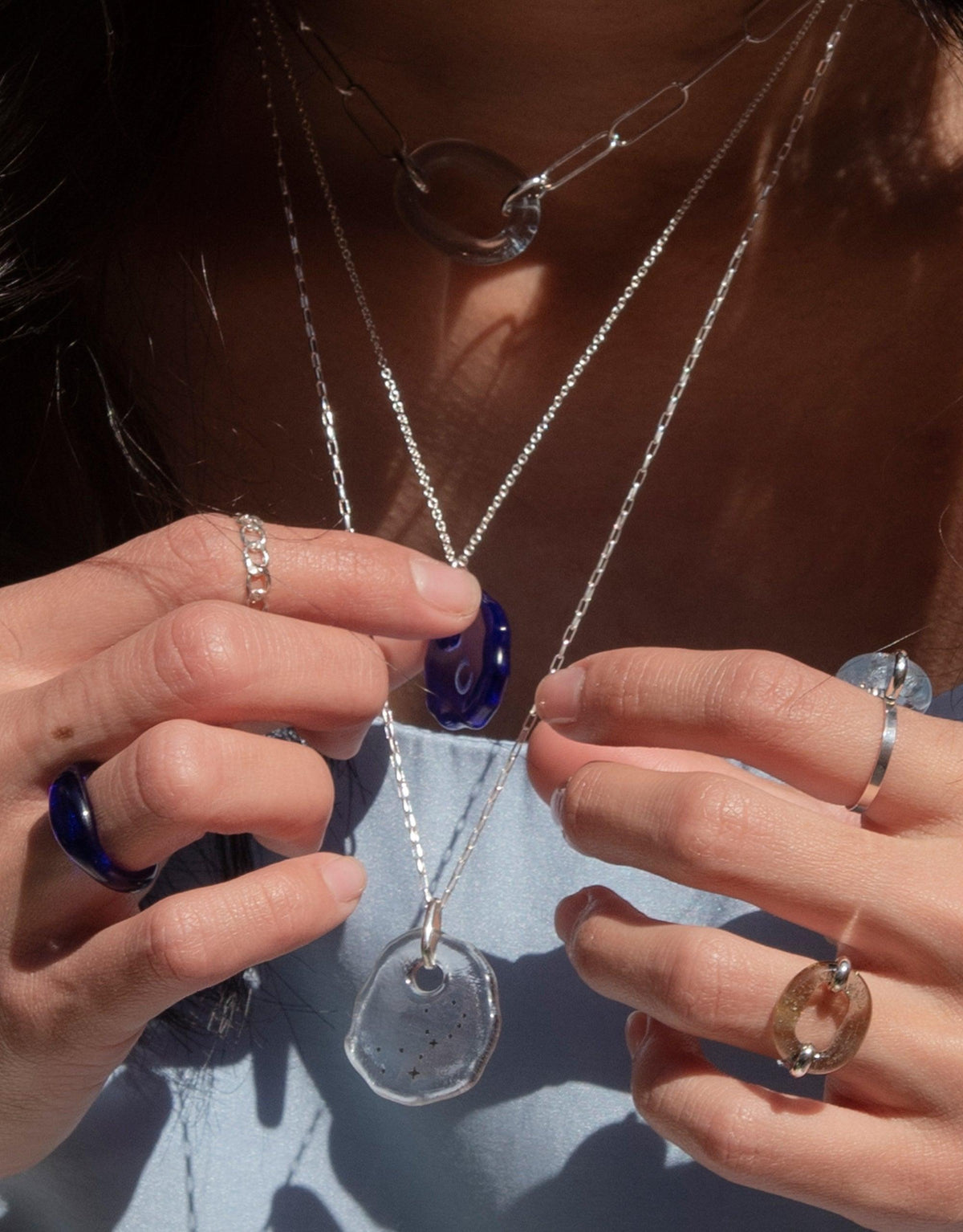 Hands displaying delicate Constellation Necklace with clear glass pendant engraved with zodiac symbols, on silver chain. Sustainable jewelry from The Messenger Collection by CLED