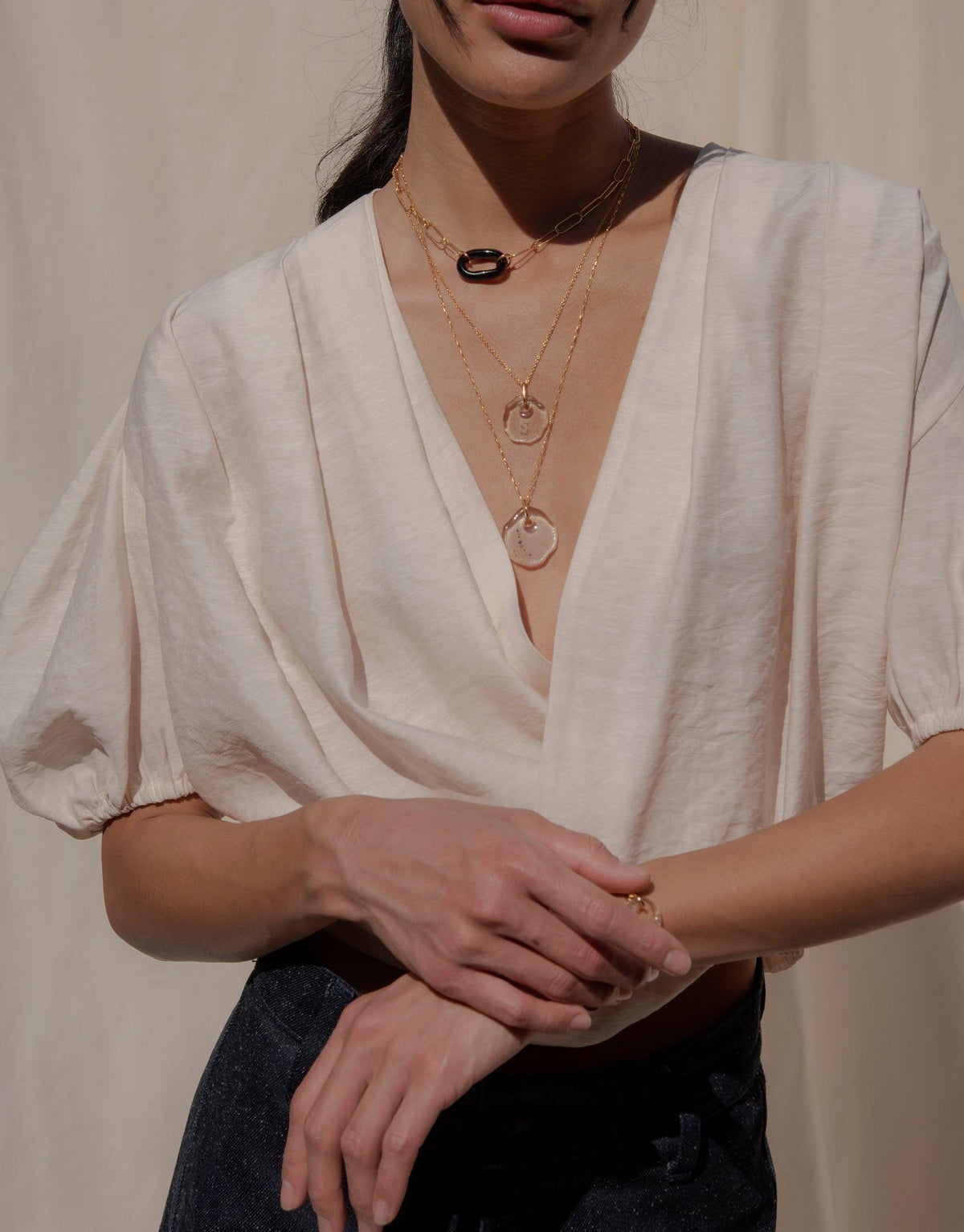 Elegant Constellation Necklace layered with delicate chains and glass pendants, featuring zodiac star engravings on organic-shaped Eco Gem. Showcased on model wearing a white wrap top, symbolizing connection and love. Handmade in Los Angeles by CLED.