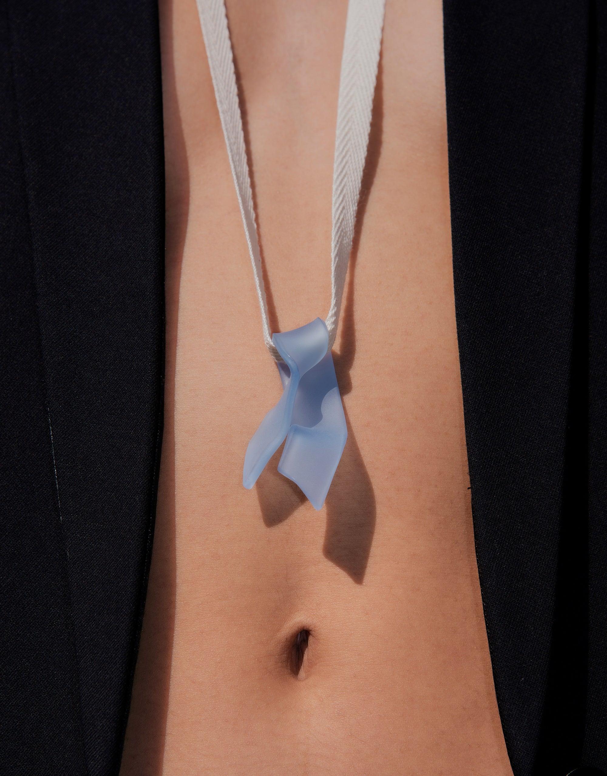 Elegant Ribbon Necklace featuring hand-formed eco gem pendant in light blue glass, suspended on white cotton ribbon against skin, showcasing unique serpentine shape and sustainable design. Handcrafted sustainable jewelry by CLED.
