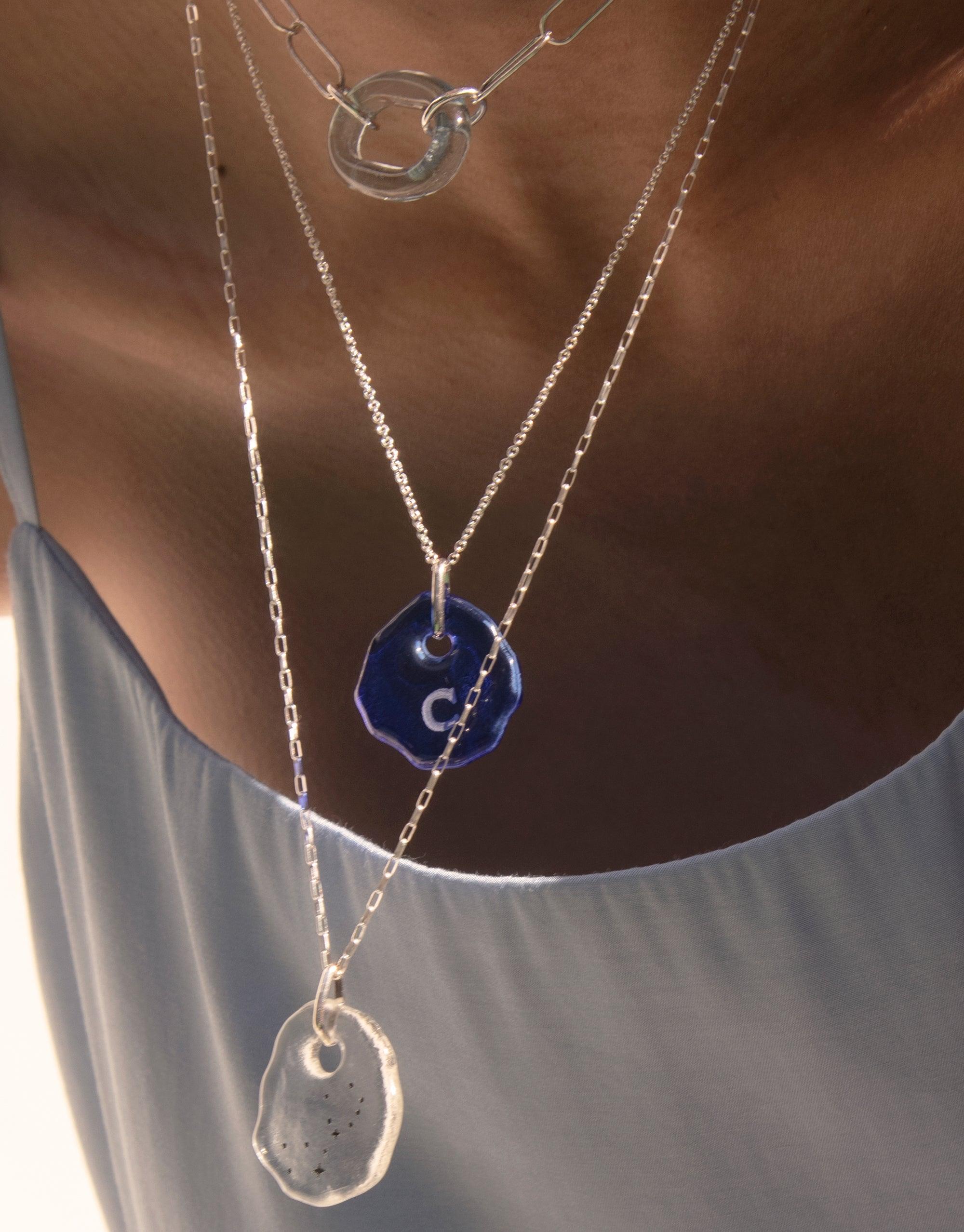 Layered necklaces featuring Messenger Necklace with Clear Engraving and eco gem pendants in blue and clear, showcasing personalized design on delicate silver chains. Sustainable jewelry for expressing sentiments and connecting with loved ones. CLED, Messenger Necklace | Clear Engraving.