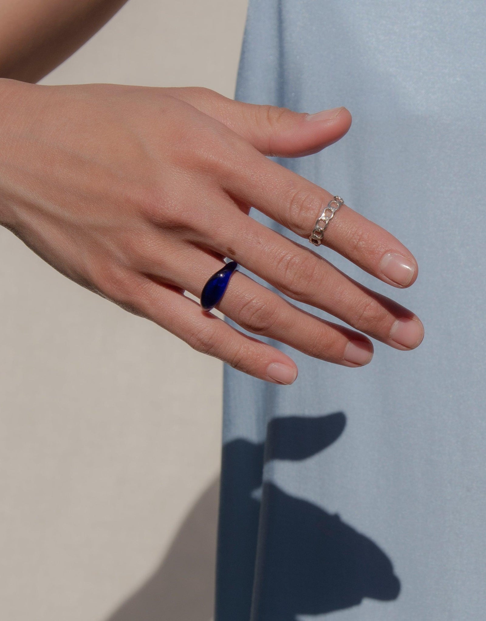 Close-up of a hand wearing an Engravable Signet Ring with a blue eco gem, showcasing the Messenger Collection's personalized design. The ring is paired with a delicate band, highlighting CLED's sustainable and stylish jewelry.